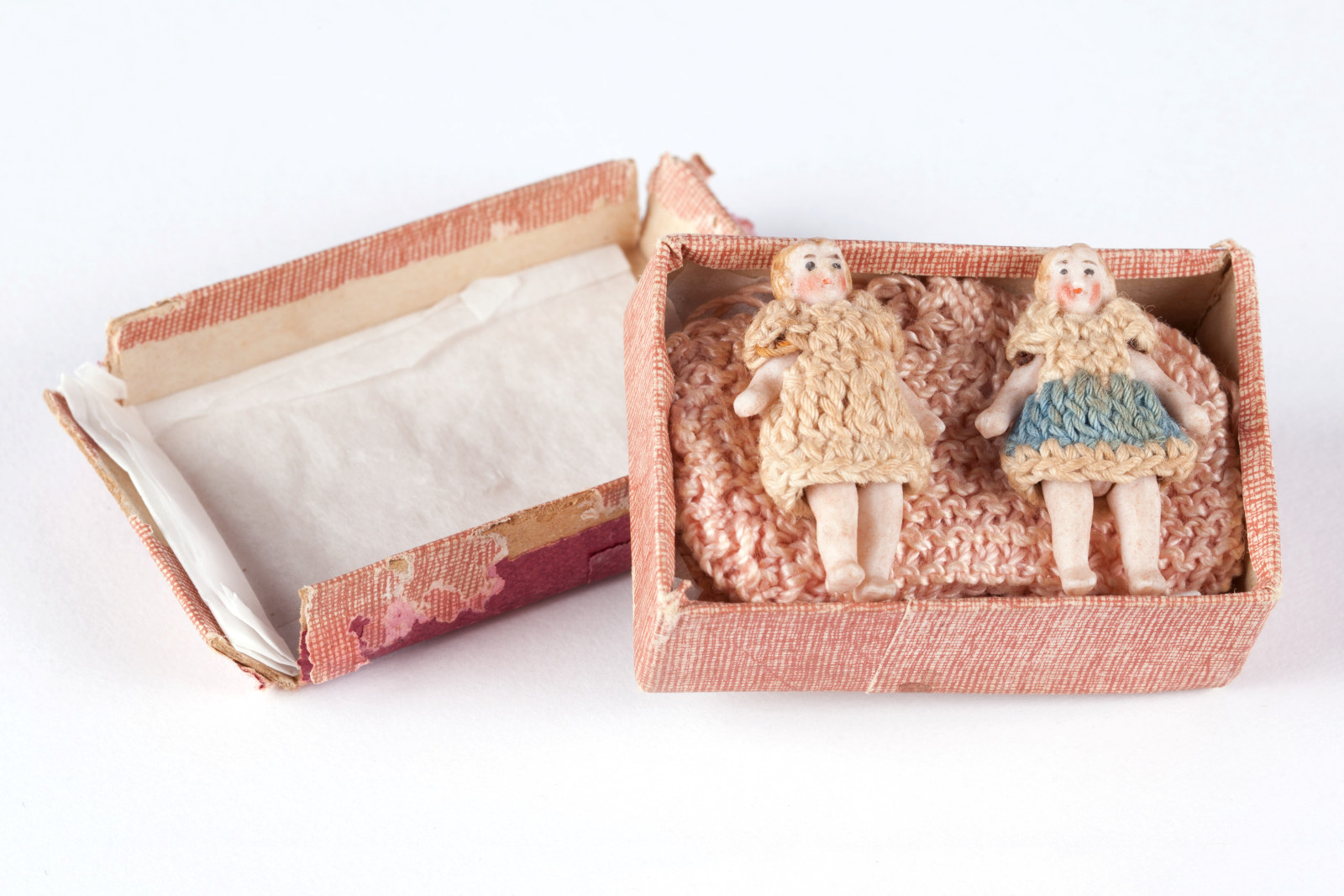 Cardboard box containing two small bisque dolls and a pair of pink knitted booties