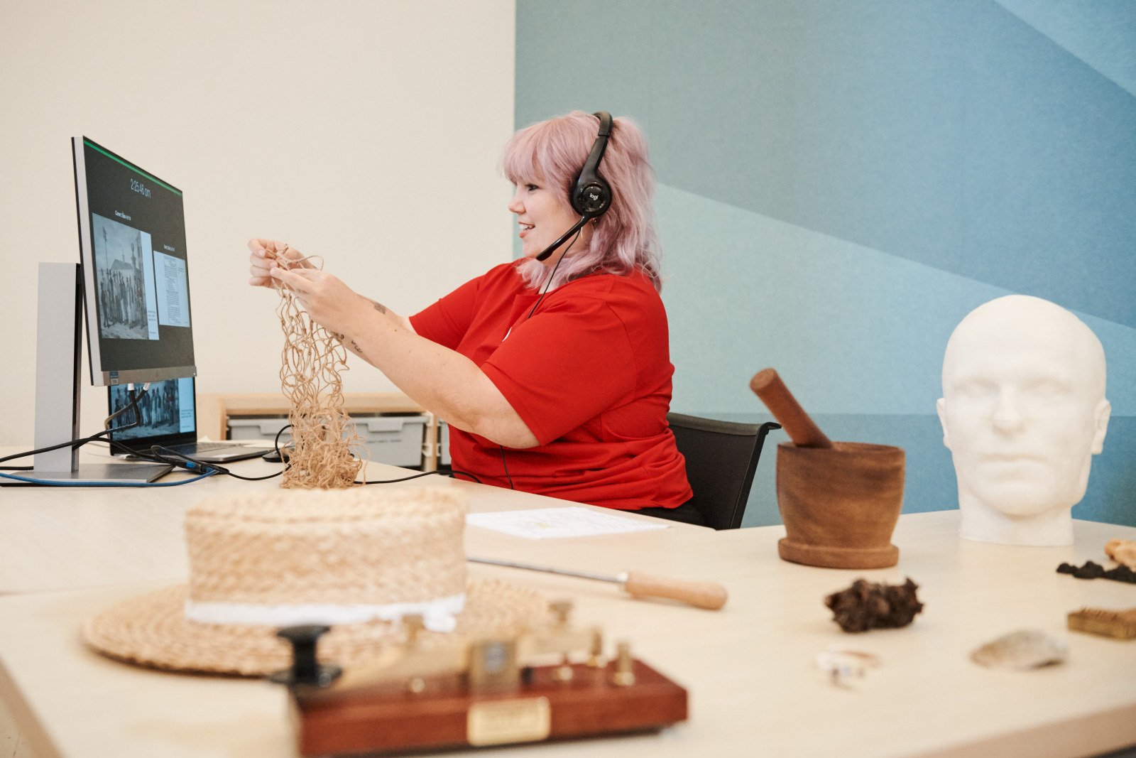 Zoe Kellam, Curriculum Program Deliverer, hosts a virtual excursion from the learning space at the Hyde Park Barracks. She sits in front of a monitor and laptop and is surrounded by historical objects.
