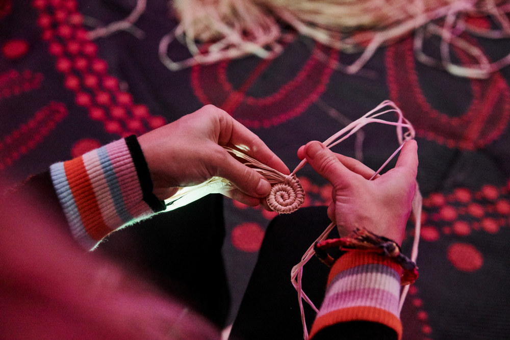 Close up of hands weaving a spiral out of dried raffia.