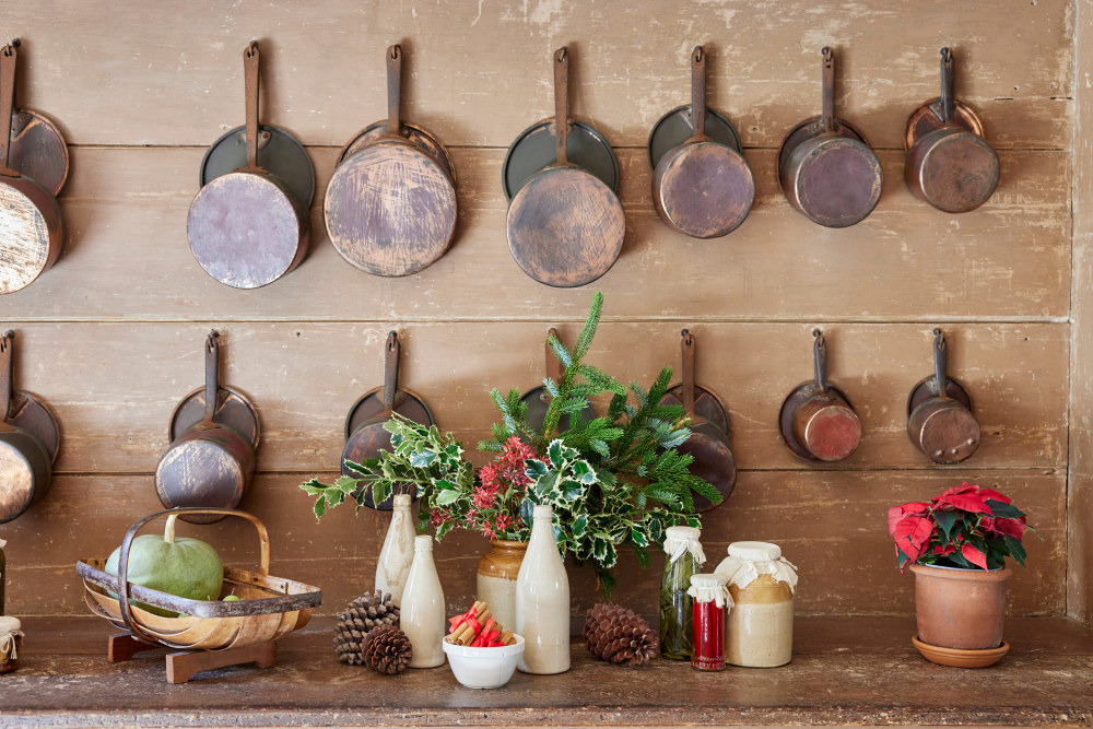 Saucepans hanging on the wall with bottles of preserves, pine cones and Christmas holly in the kitchen at Vaucluse House
