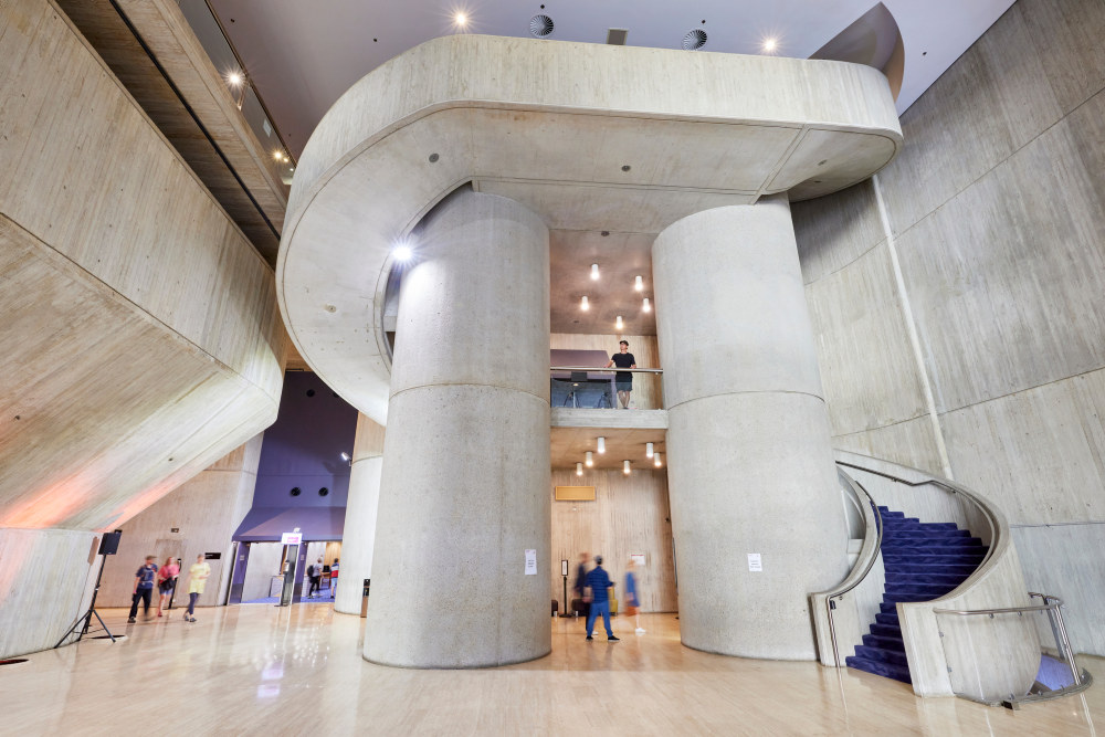 Wide shot of the foyer of the Sydney Masonic Centre, featuring a massive concrete staircase and elevator shafts.