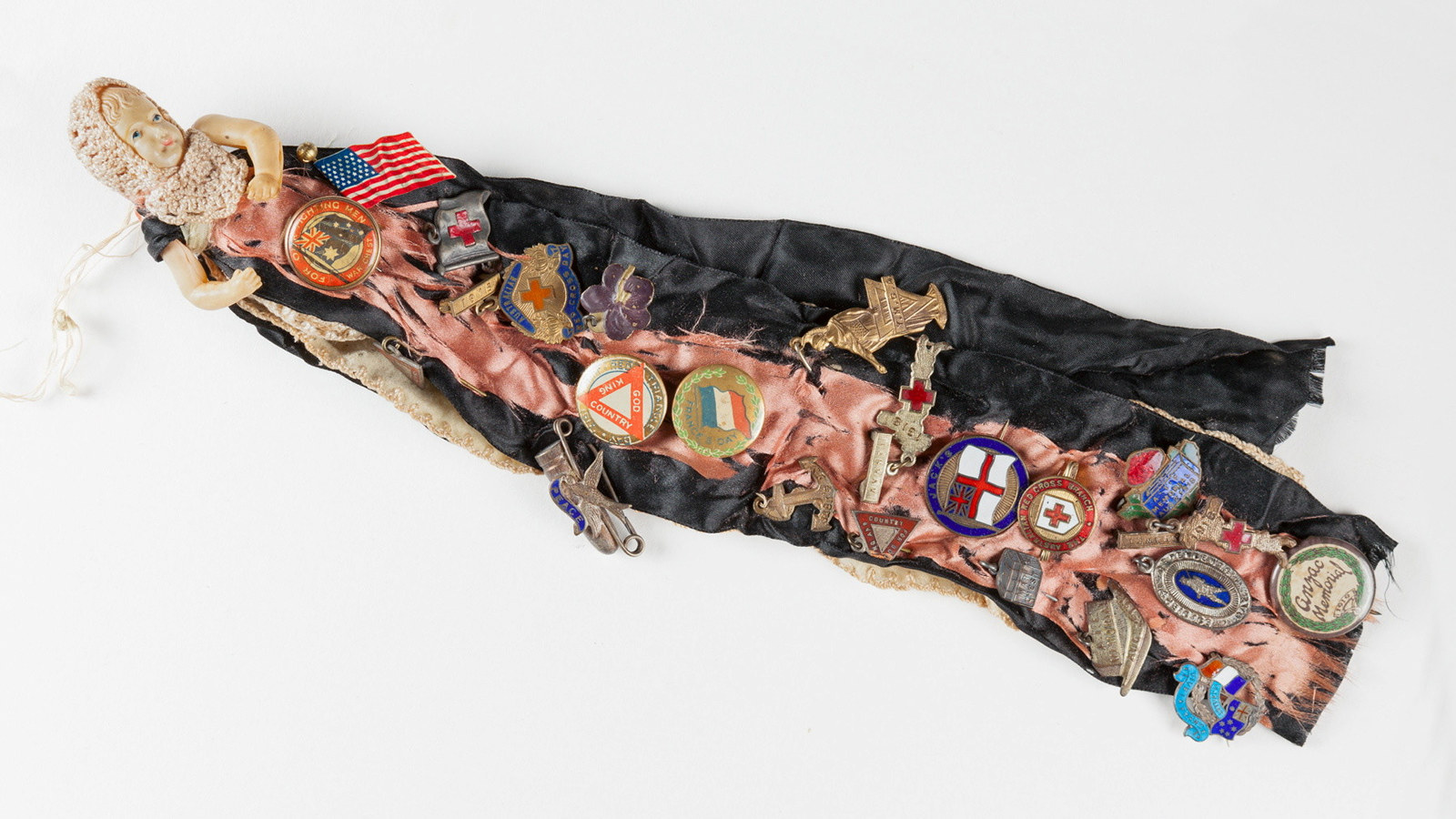 Celluloid doll wearing garment pinned with variety of patriotic badges.