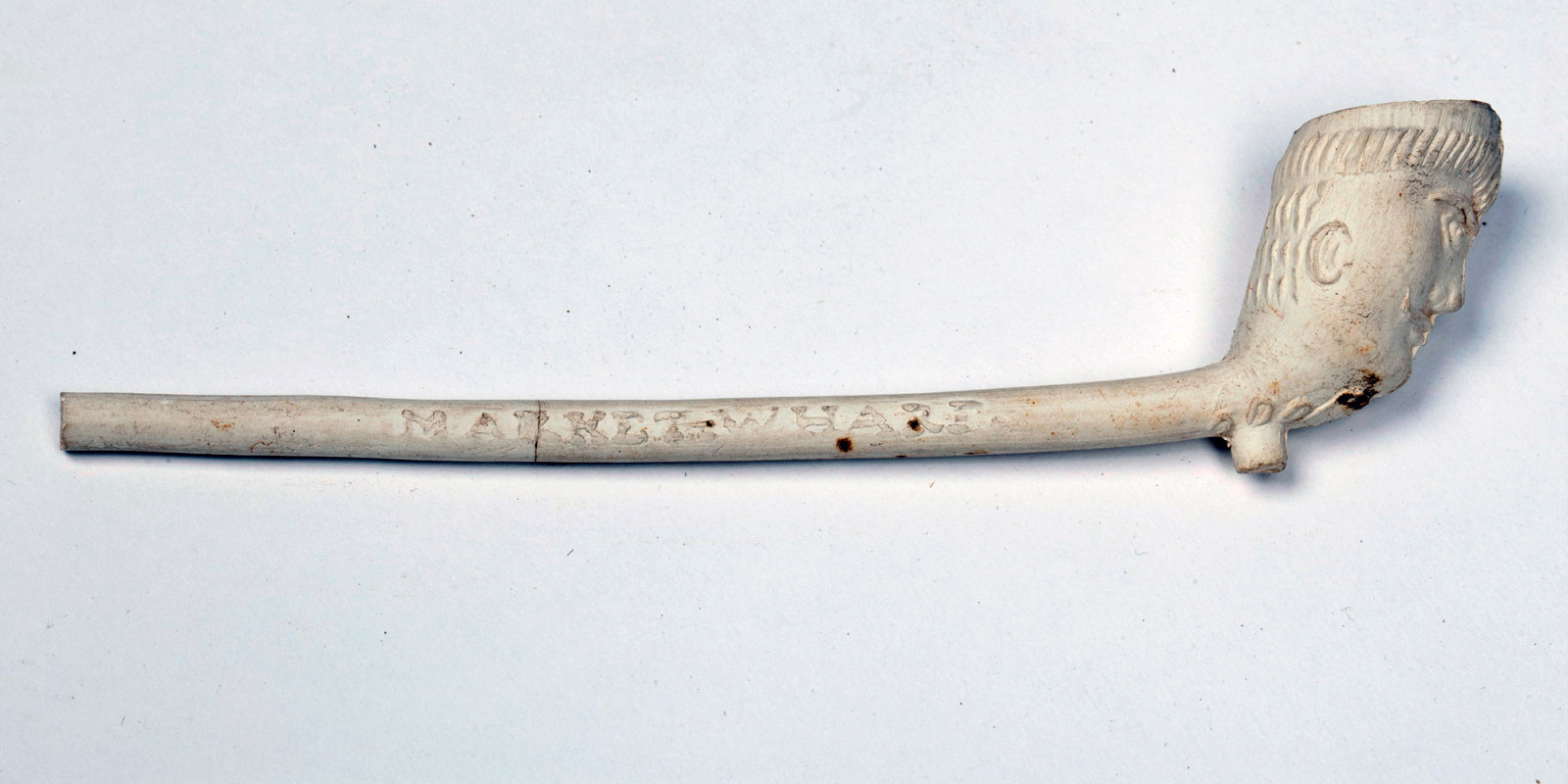 Slender-stemmed white clay pipe with carved bowl and lettering on stem.