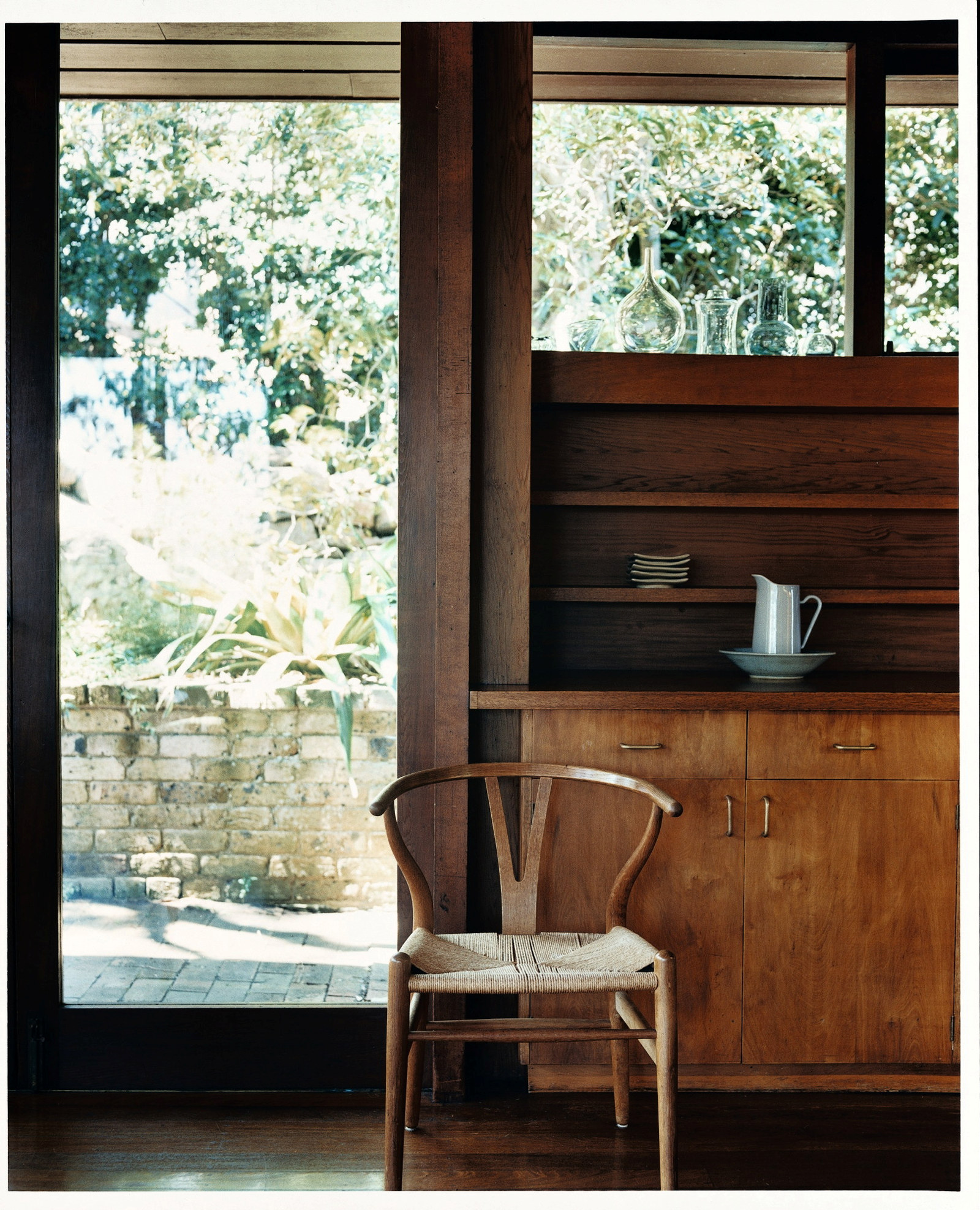 This is a photograph of a specially designed timber chair sitting in front of a timber cupboard and glass door