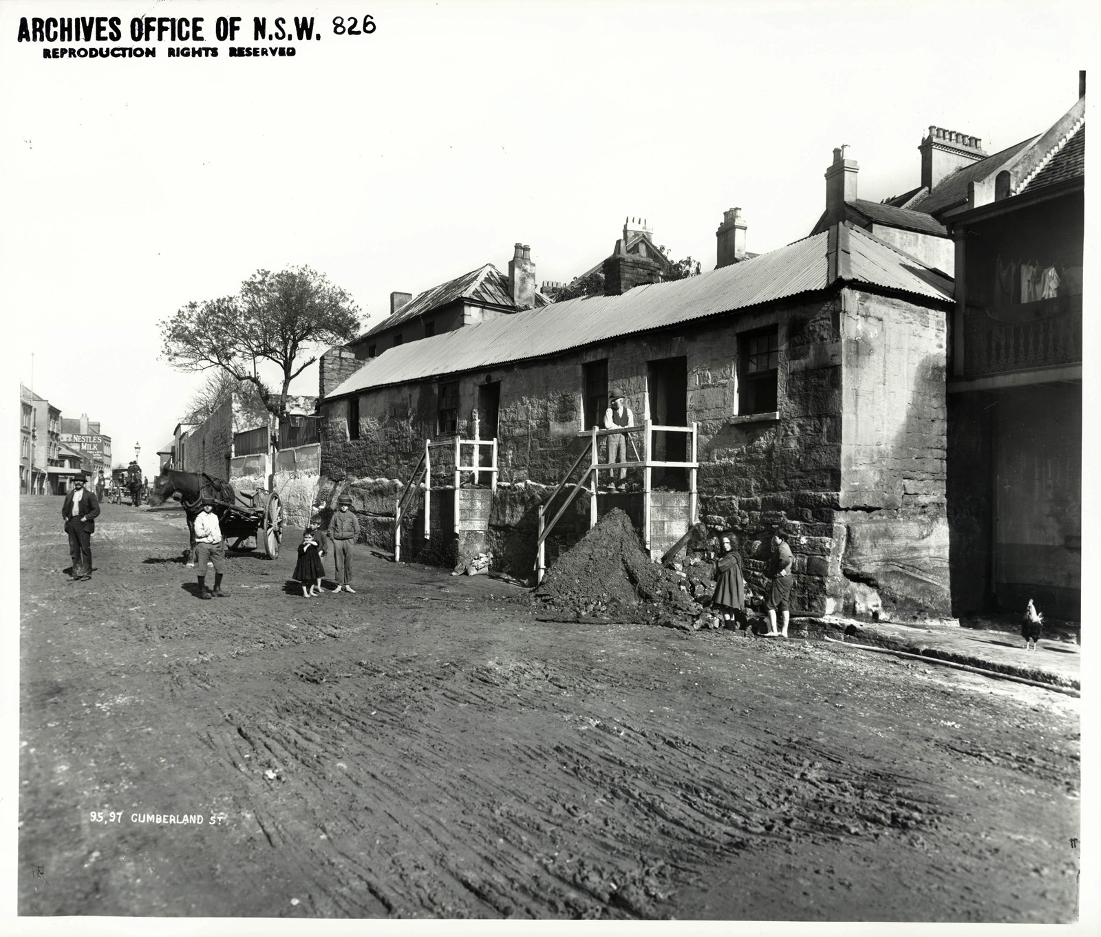 Photograph of a row of small cottages lining a dirt street. Children are shown standing on the street.