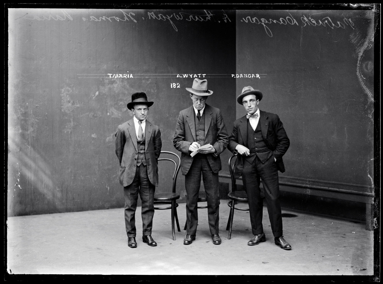 Black and white mugshot of three standing men.