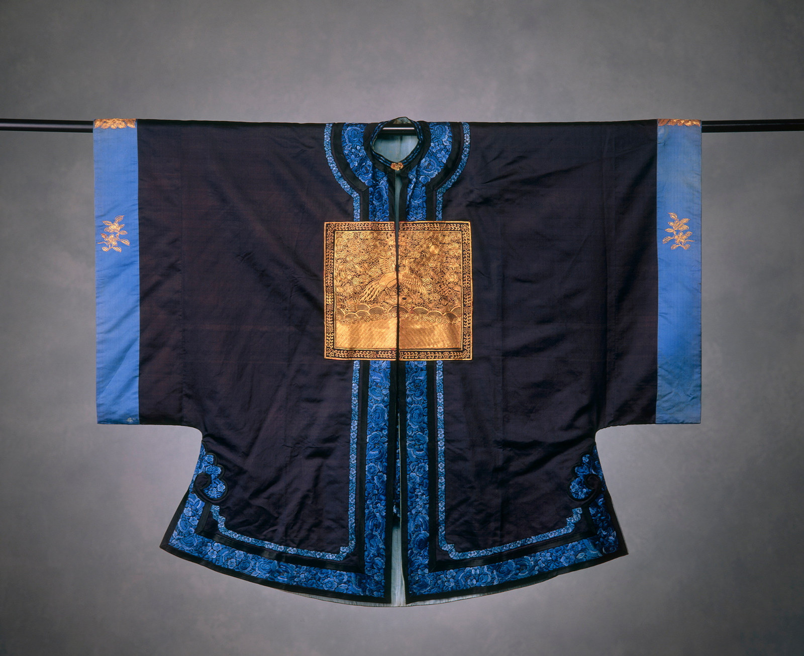 Navy coloured Chinese coat, trimmed with lighter blue bands, with golden emblems. The coat features a bold golden square panel in the centre of the chest.