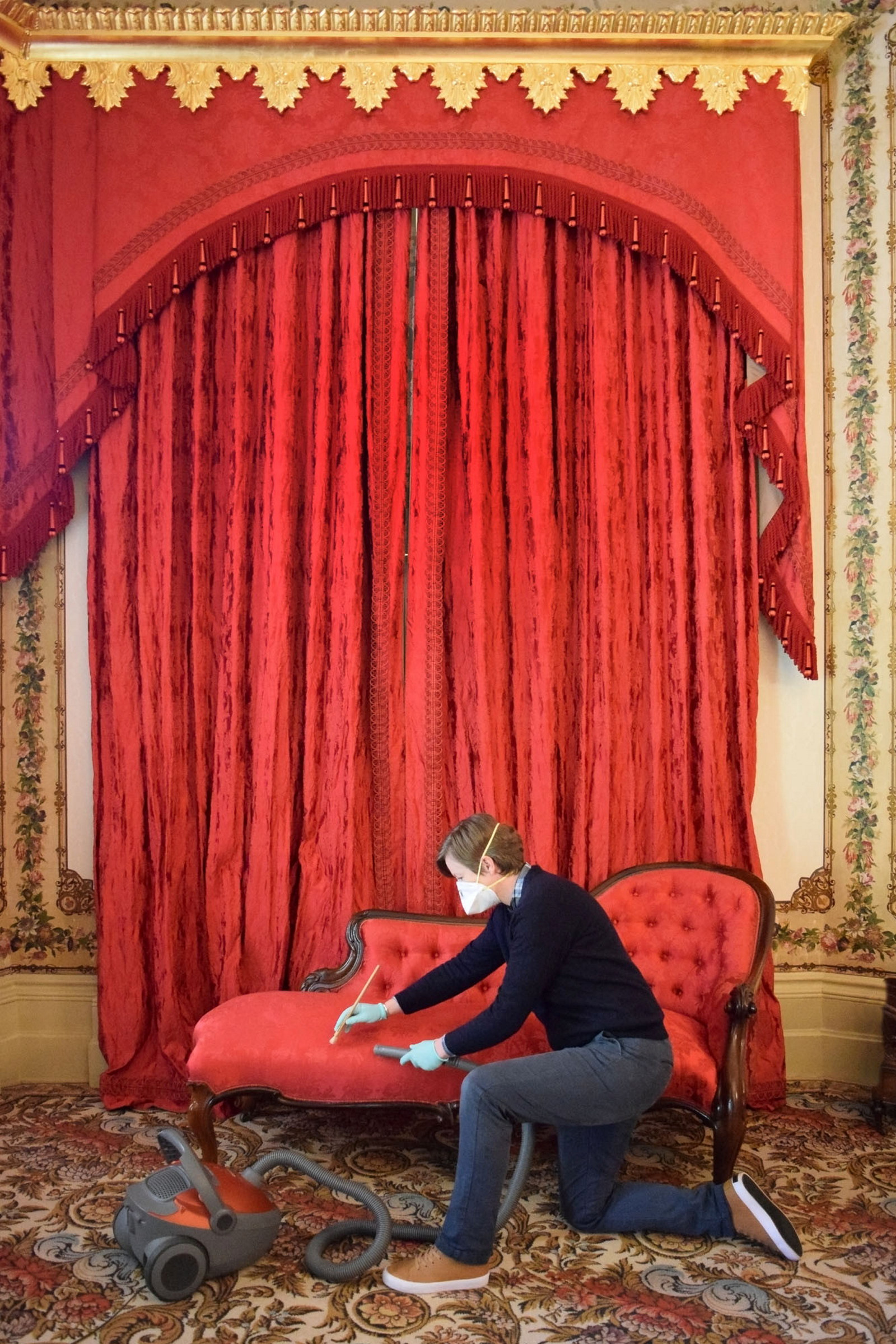 Person kneeling in front of red furniture and drapes.