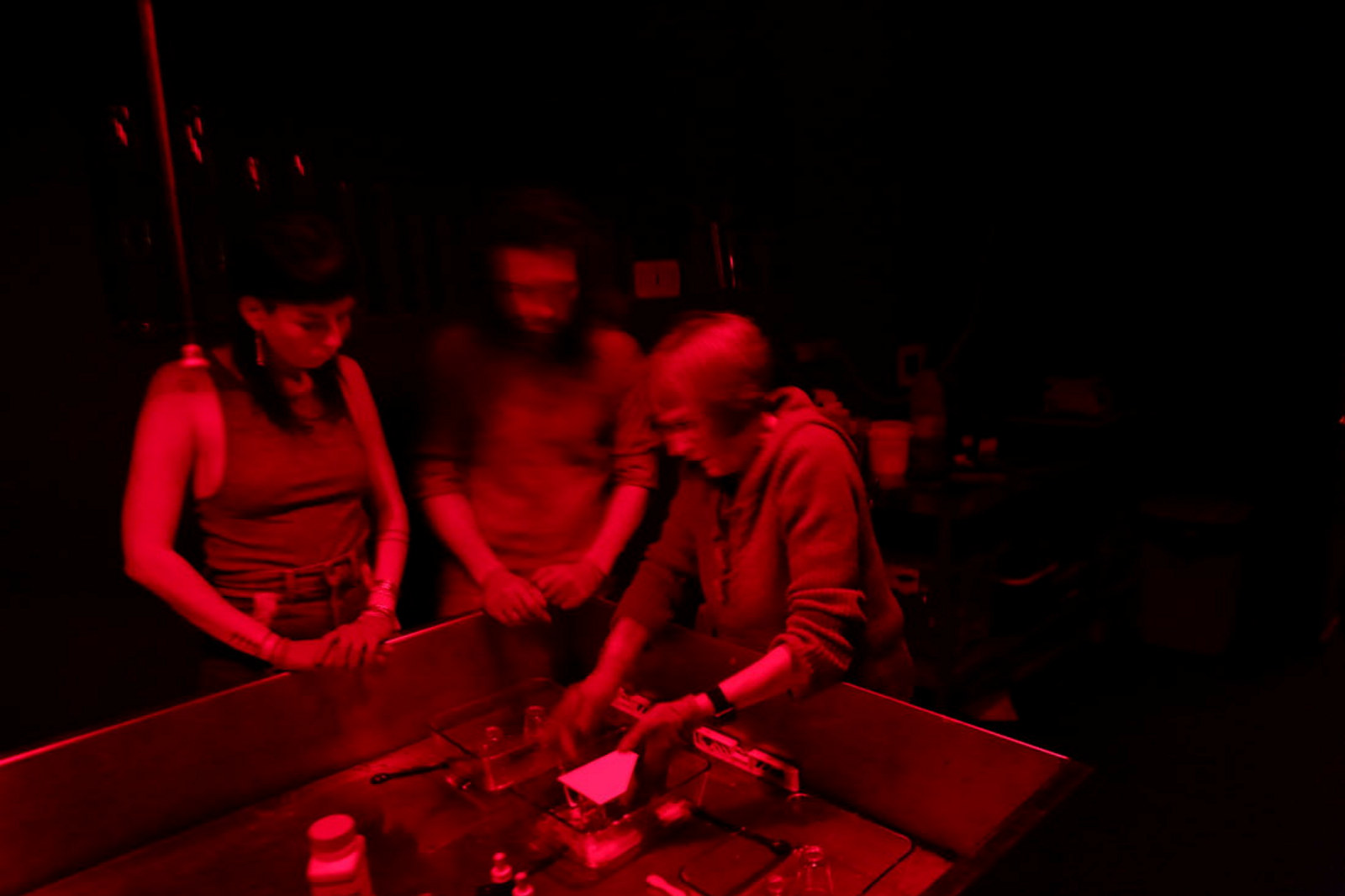 Group in red-lit darkroom working with glass plates and emulsion.