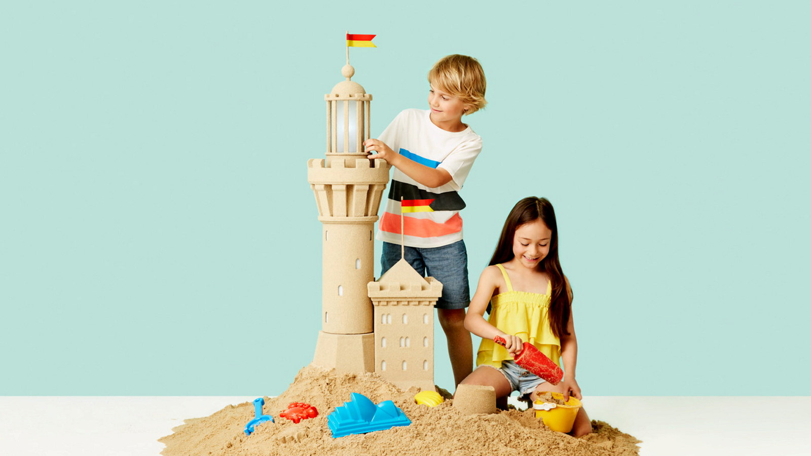 A young boy and girl play with a sand castle tower