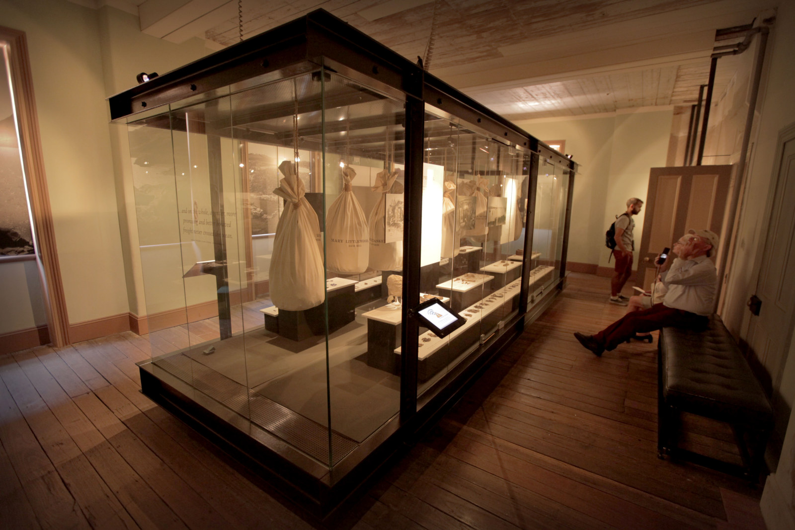 Image of a large glass showcase that fills a room. Sacks can be seen hanging inside.