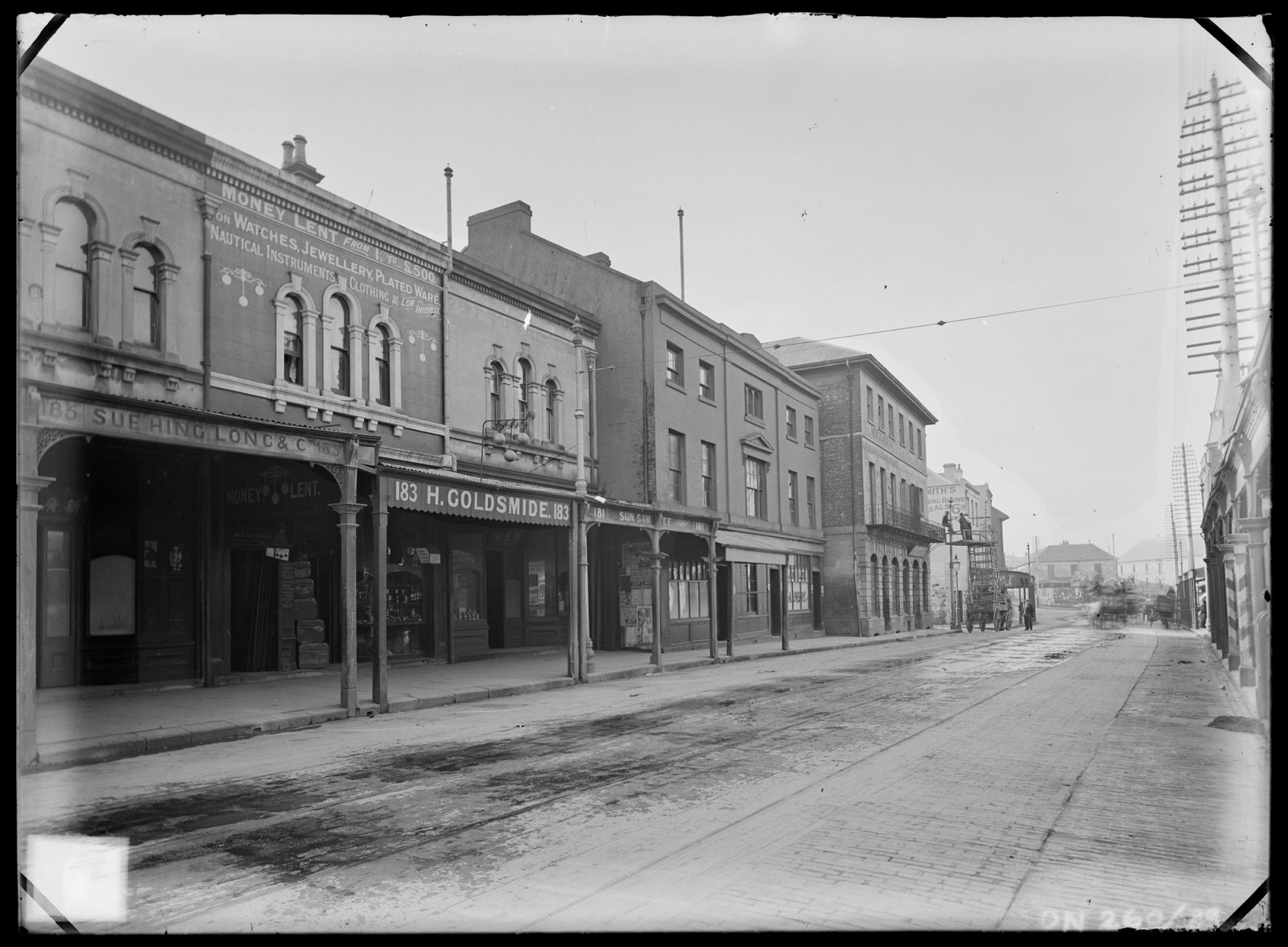 This is a black and white photograph of an empty street with shopfronts and covered awnings.