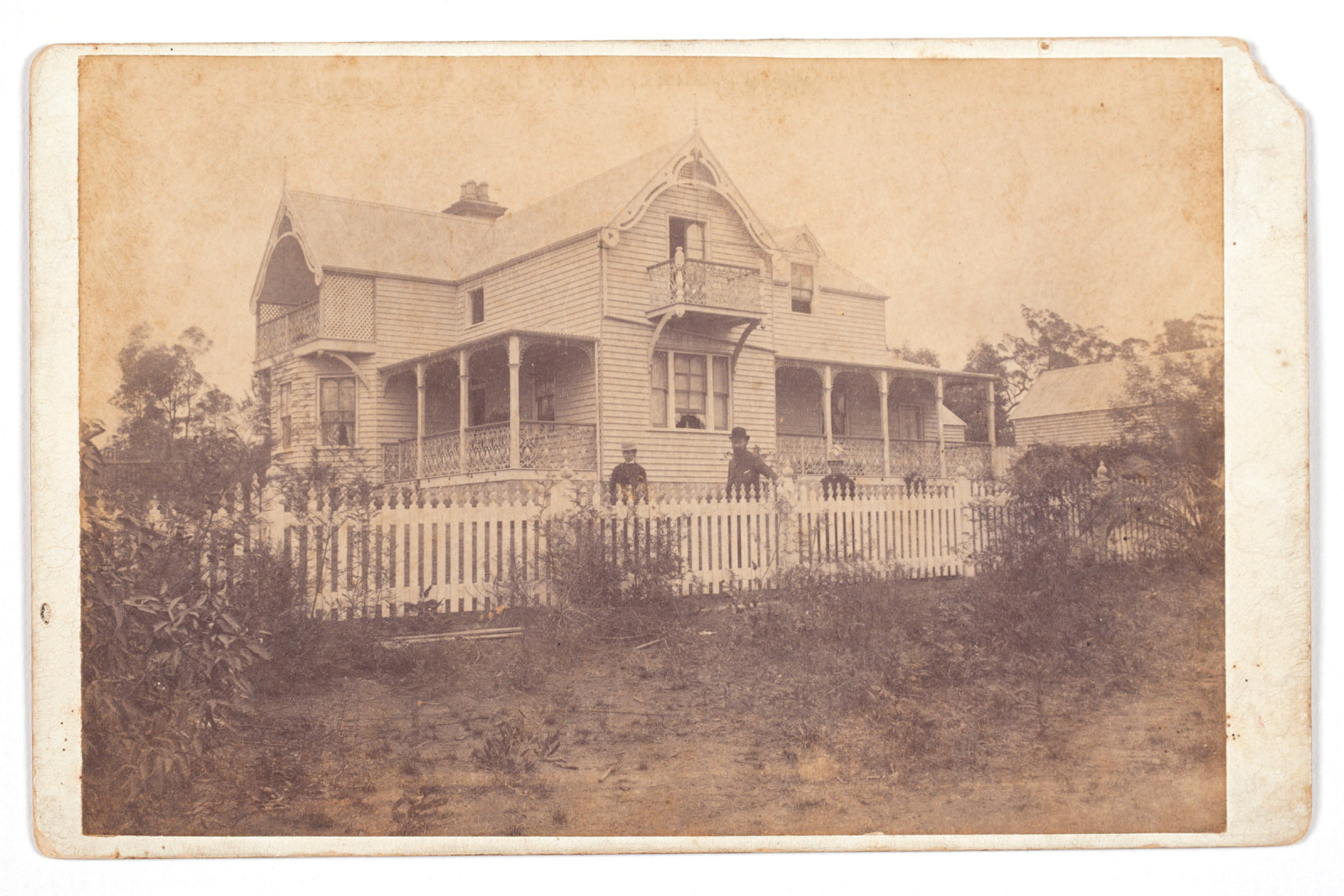 Sepia toned photo of Meroogal house exterior with three figures behind fence.