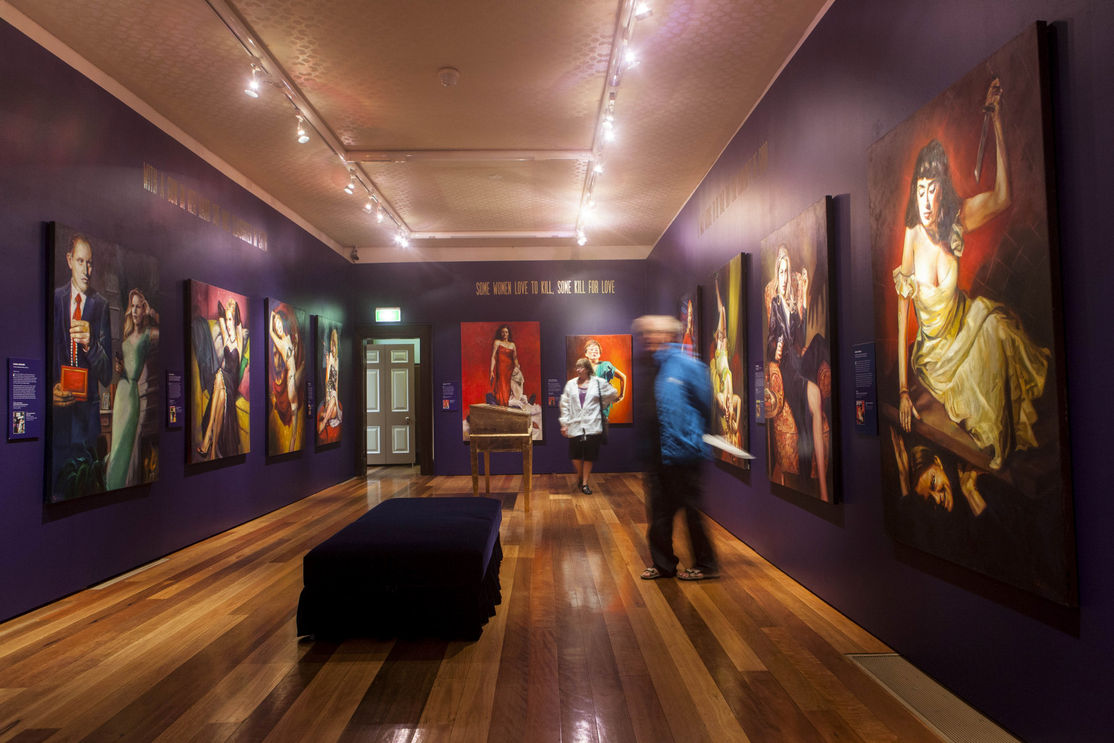 Interior view of exhibition space showing purple walls with a range of paintings hung on them.