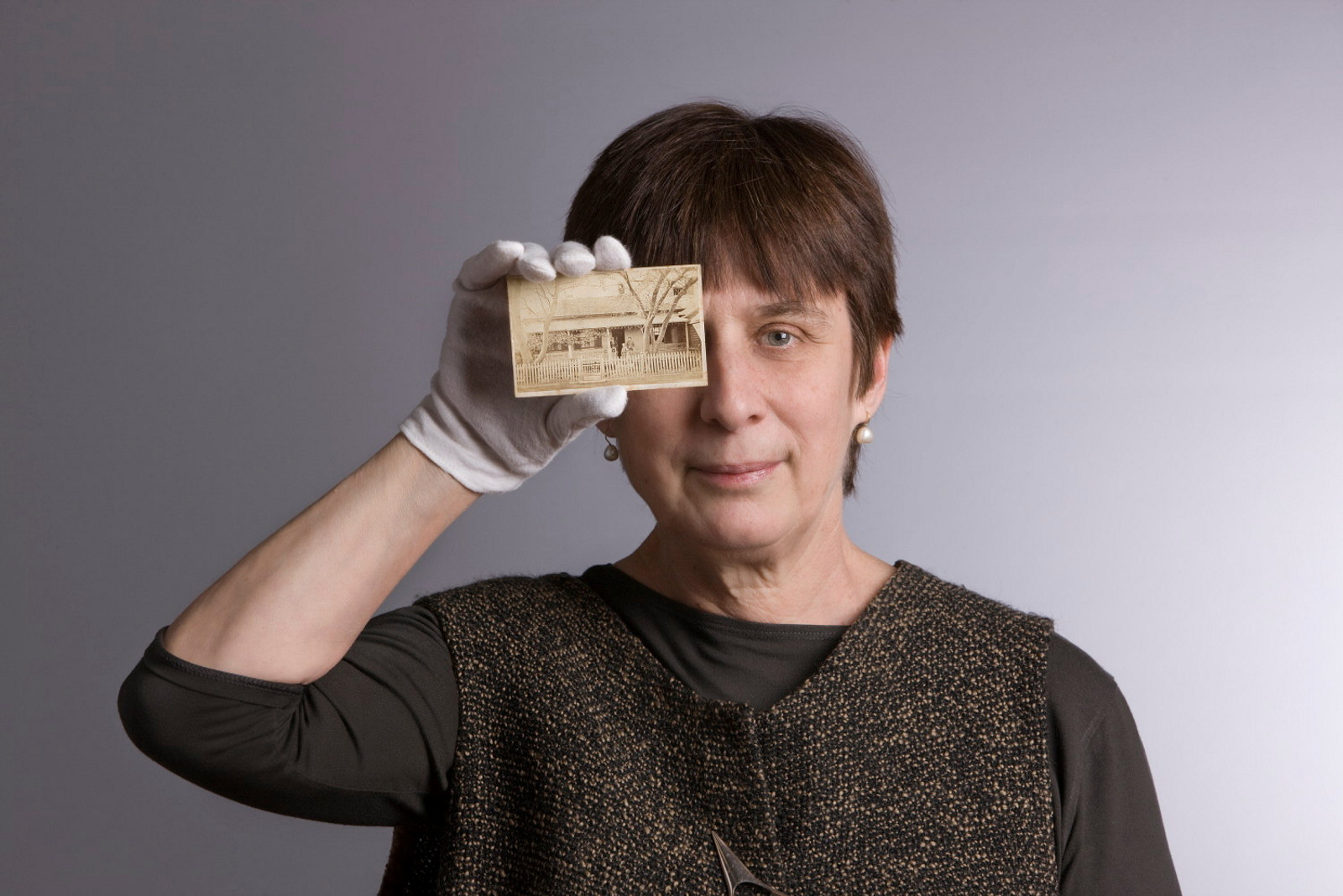 Head and shoulders photo of woman holding up card to face with conservator's white glove on hand.