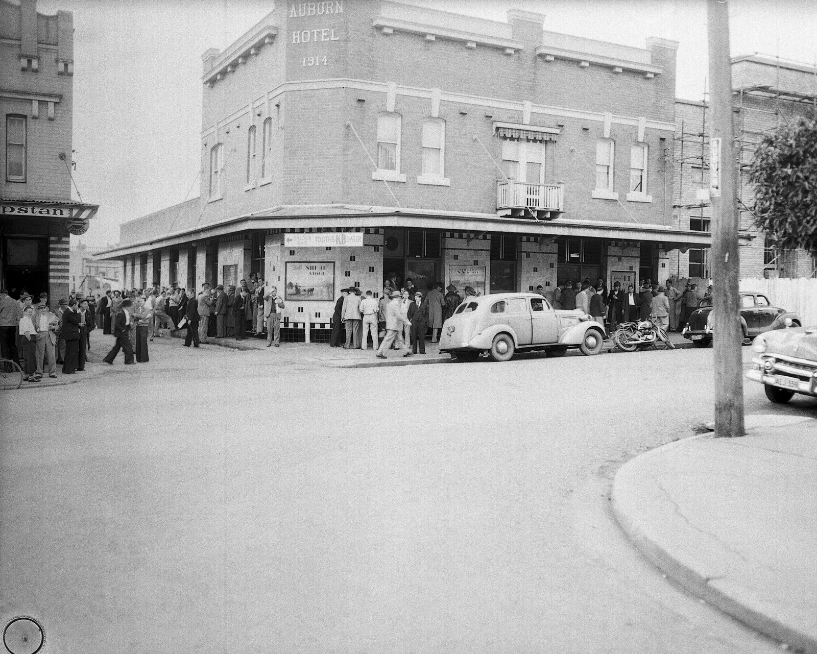 Outside of the Auburn Hotel showing a car and crowd gathered on the footpath