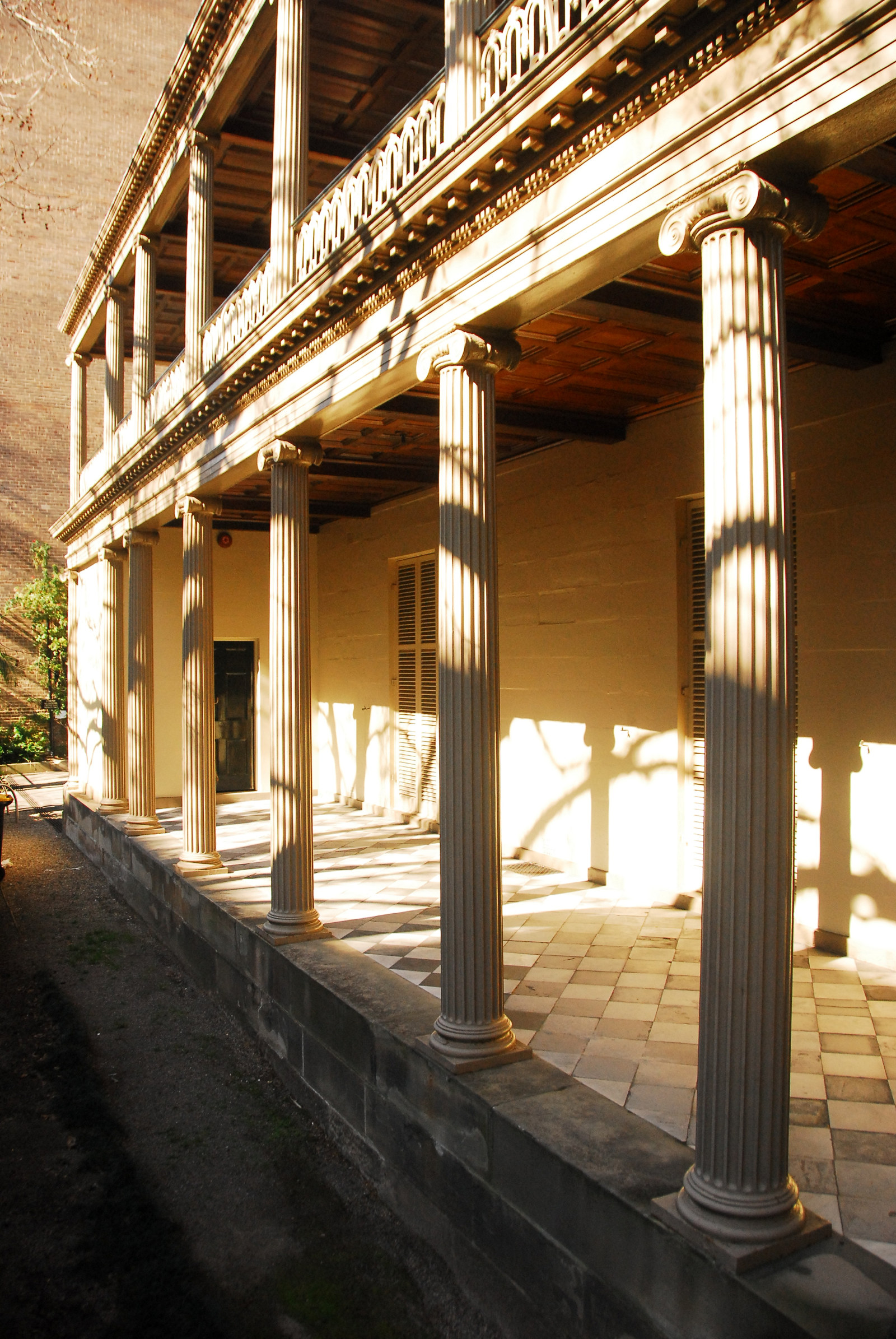 Exterior of two storey building, with columns, sunlit porch area and verandah above.