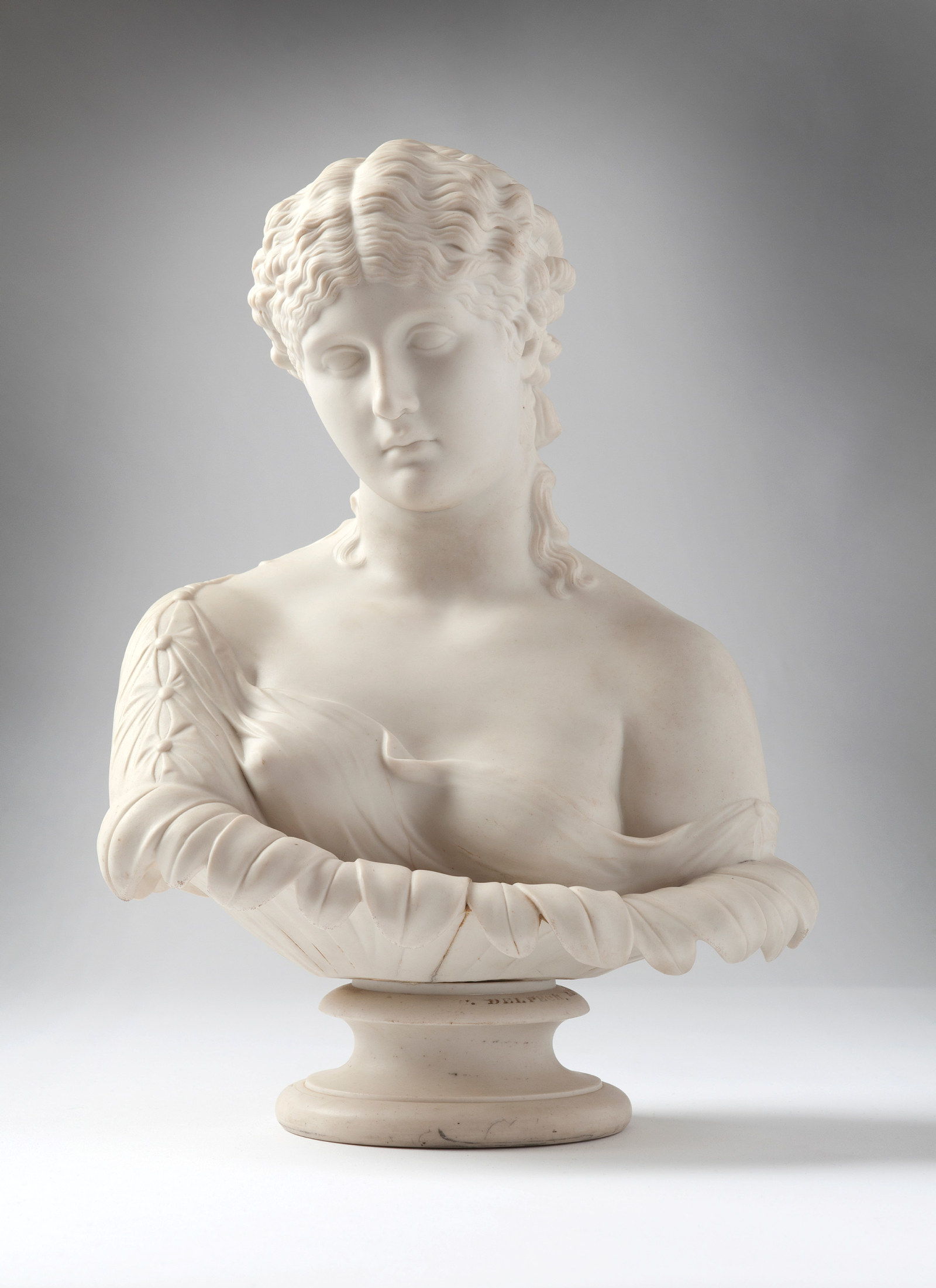 White bust of young woman on pedestal, one shoulder bare, the other draped.