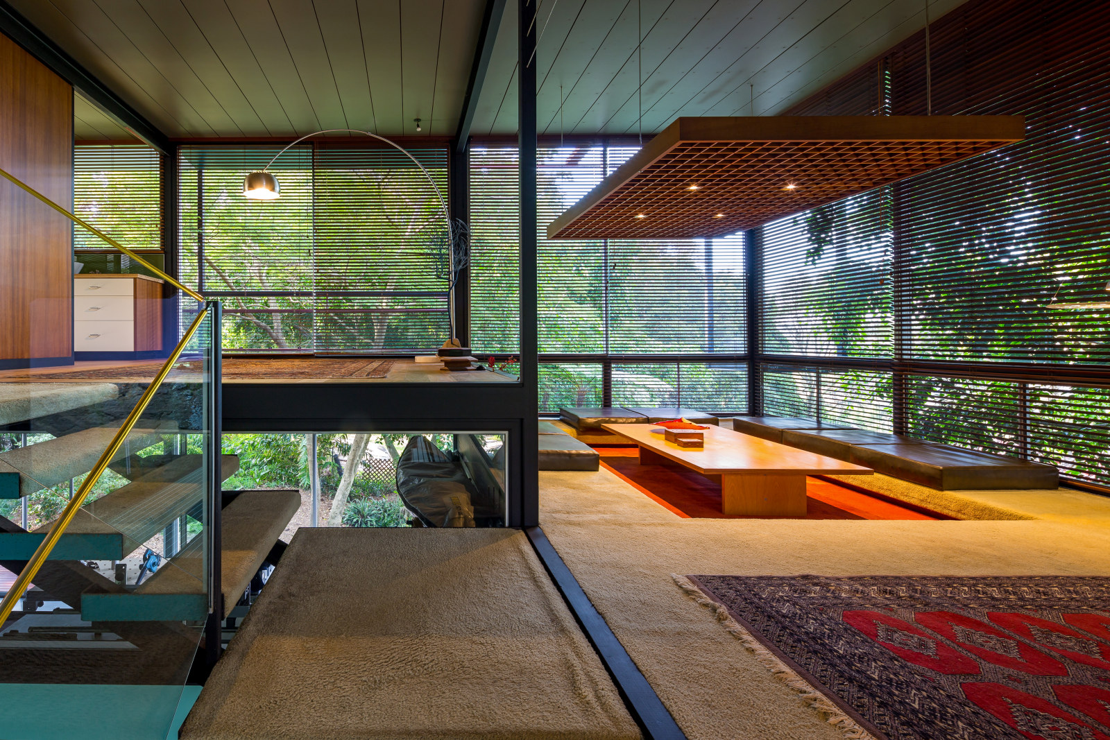 Photo looking across the interior of a modernist house. A stair can be seen and a sunken dining area.