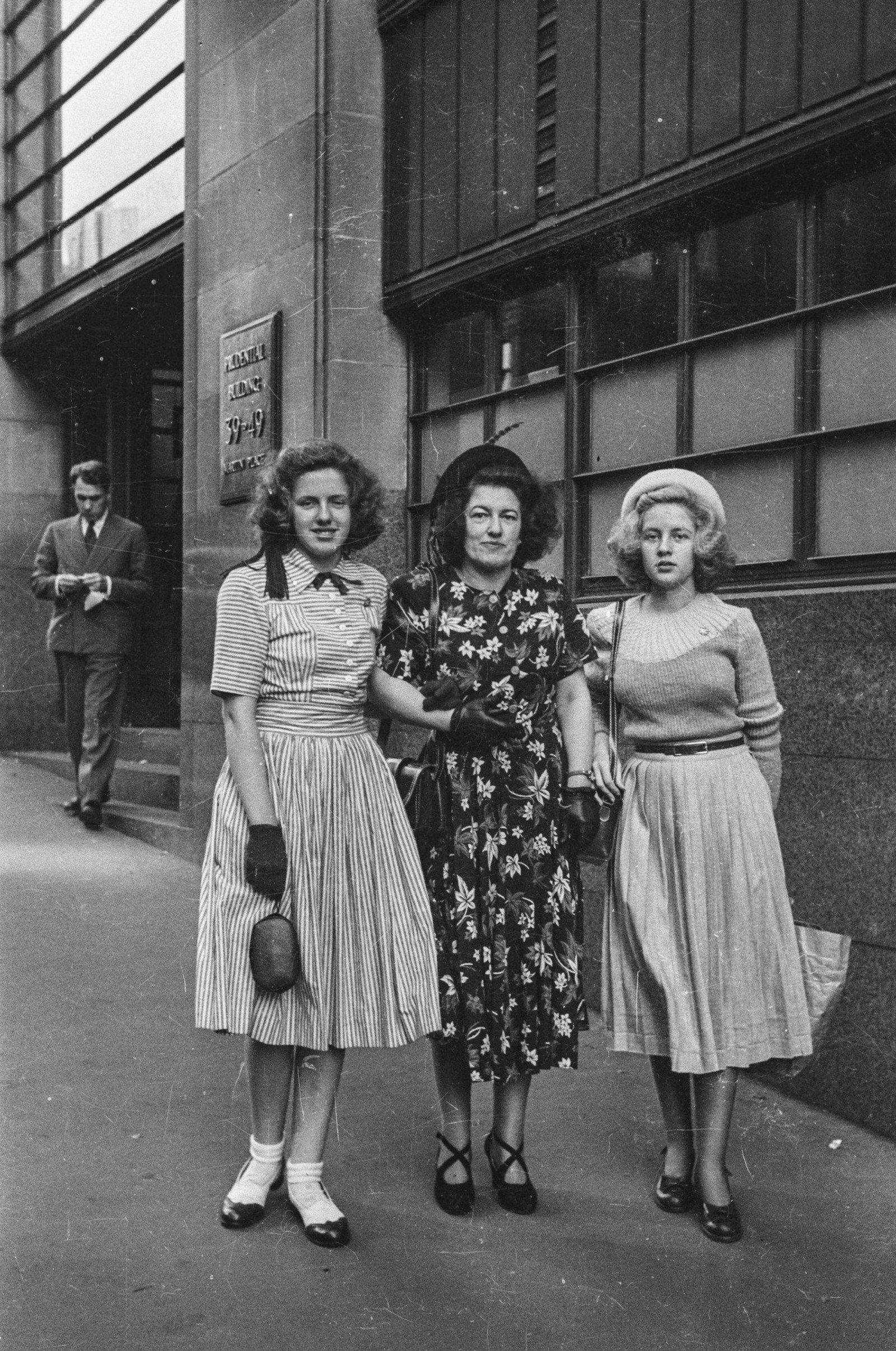 Black and white street photograph of three women linking arms standing in the street.