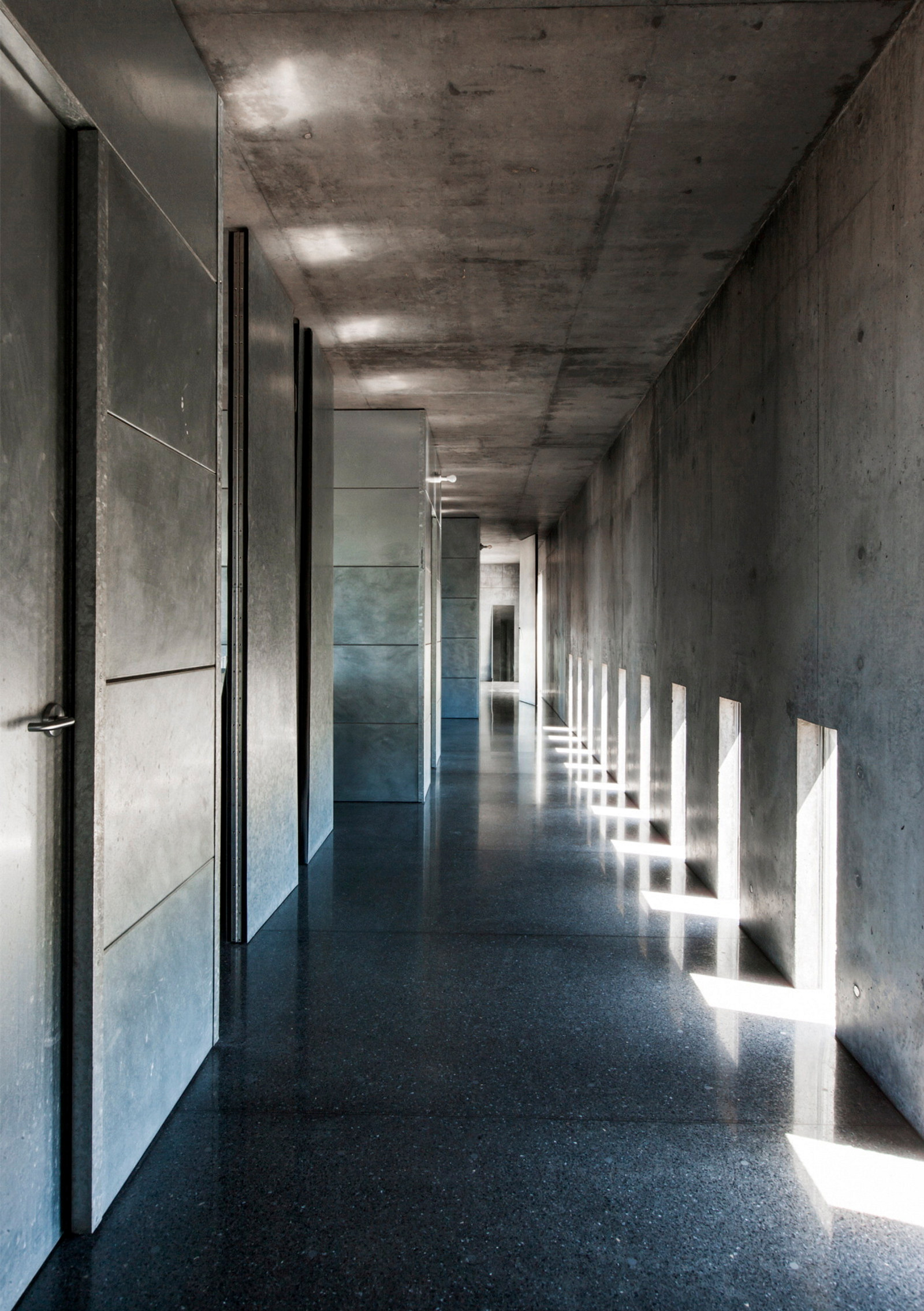 This is a colour photograph of a concrete corridor and polished floor with shafts of light entering through small low windows running the length of the corridor