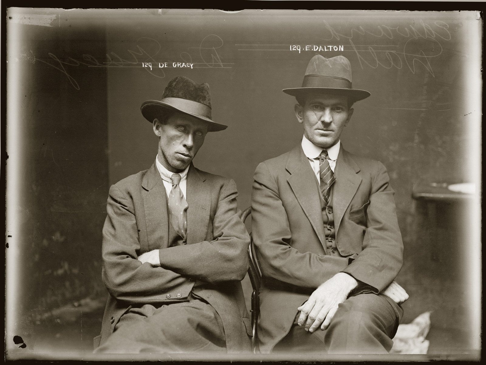 Black and white photograph of twoseated men dressed in hats and suits looking quite defiantly at the camera.