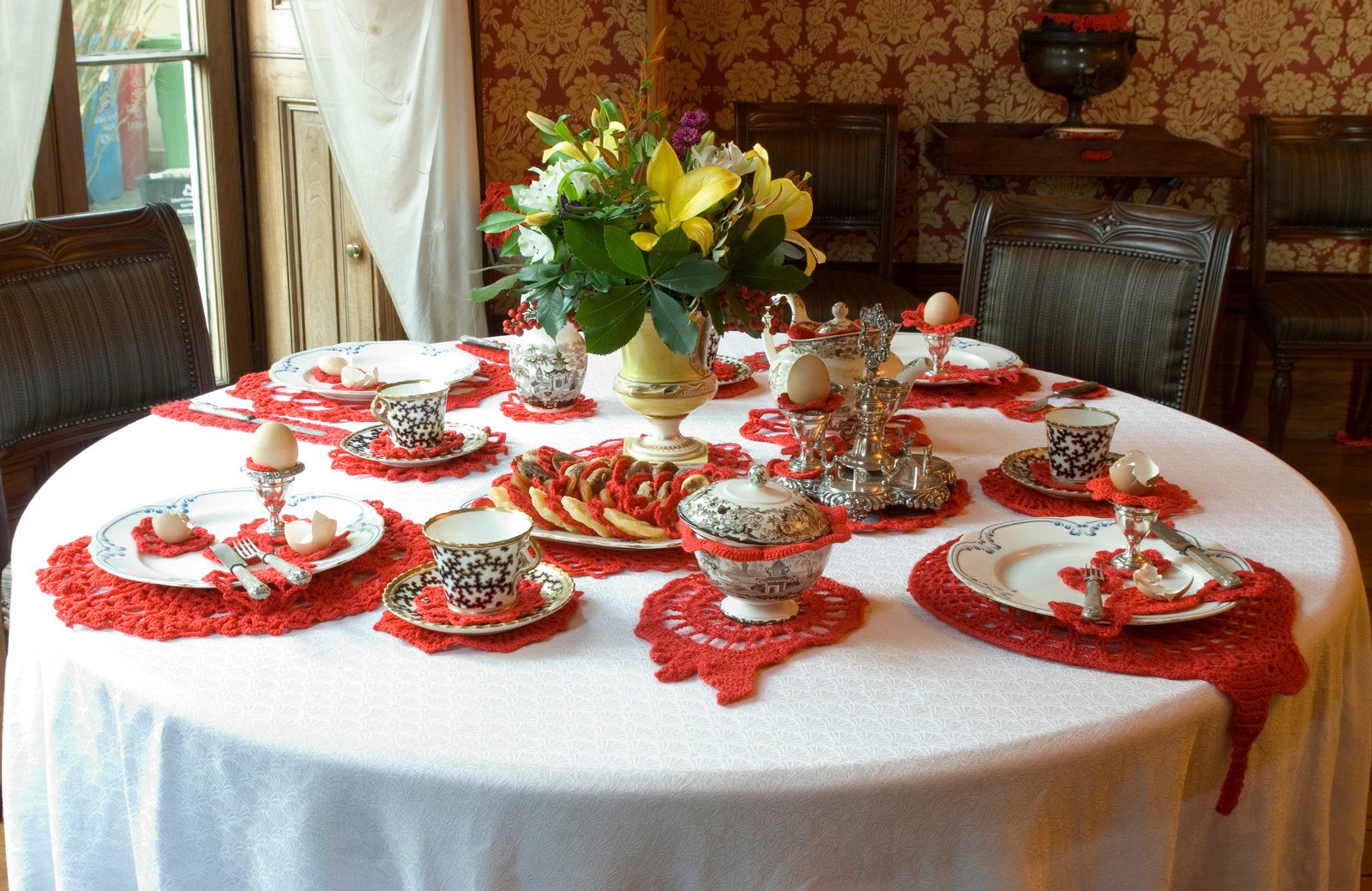 Red doilies sit under a formal 19th century tea set