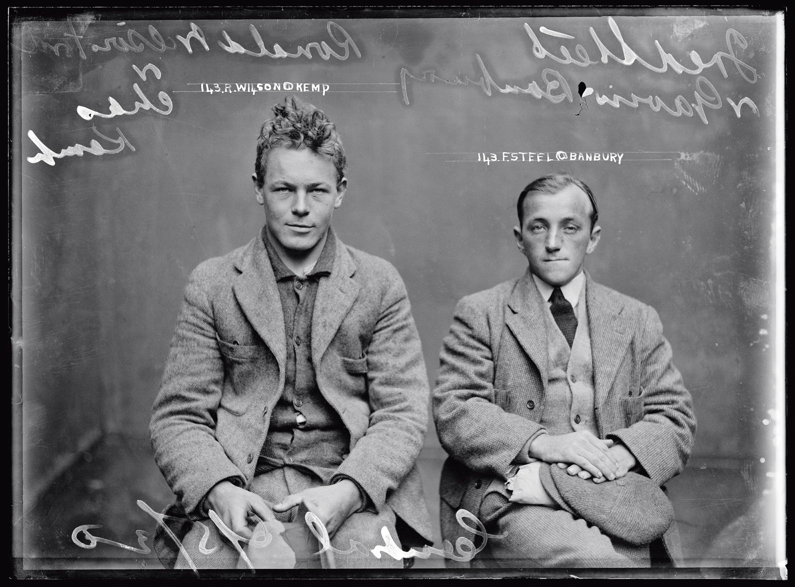 Black and white mugshot of two seated men.