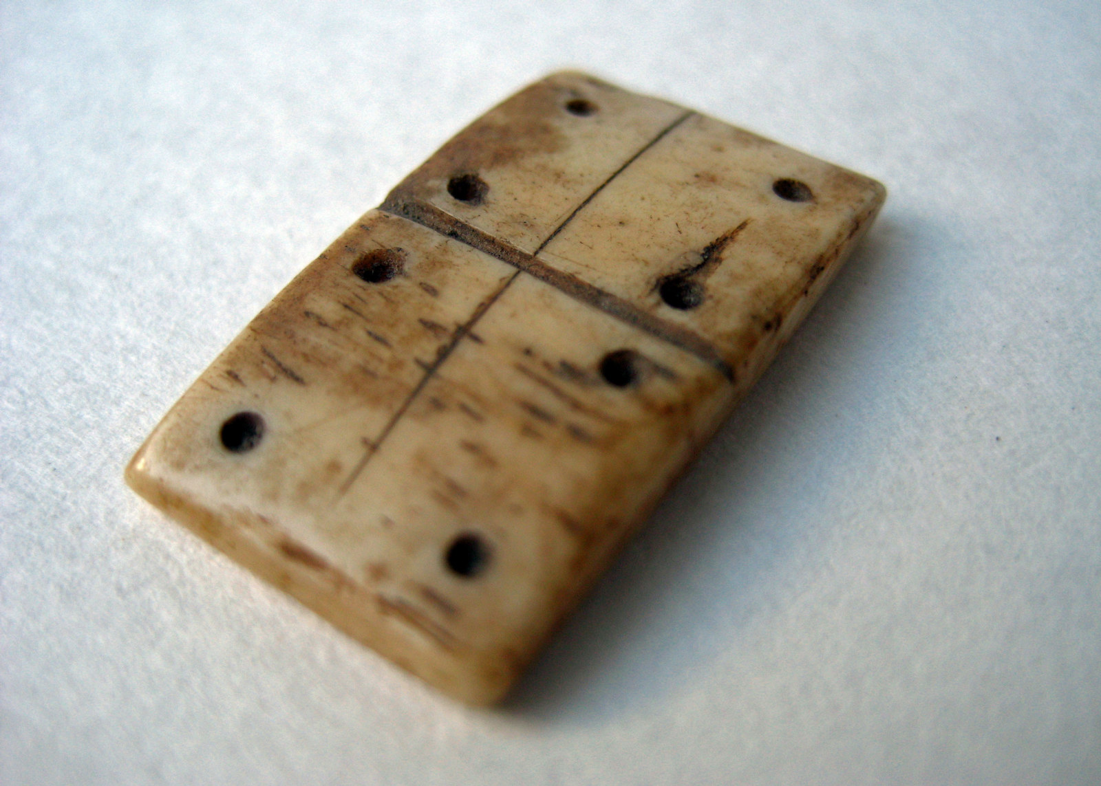Domino game piece carved from bone showing double 4 dots on white background