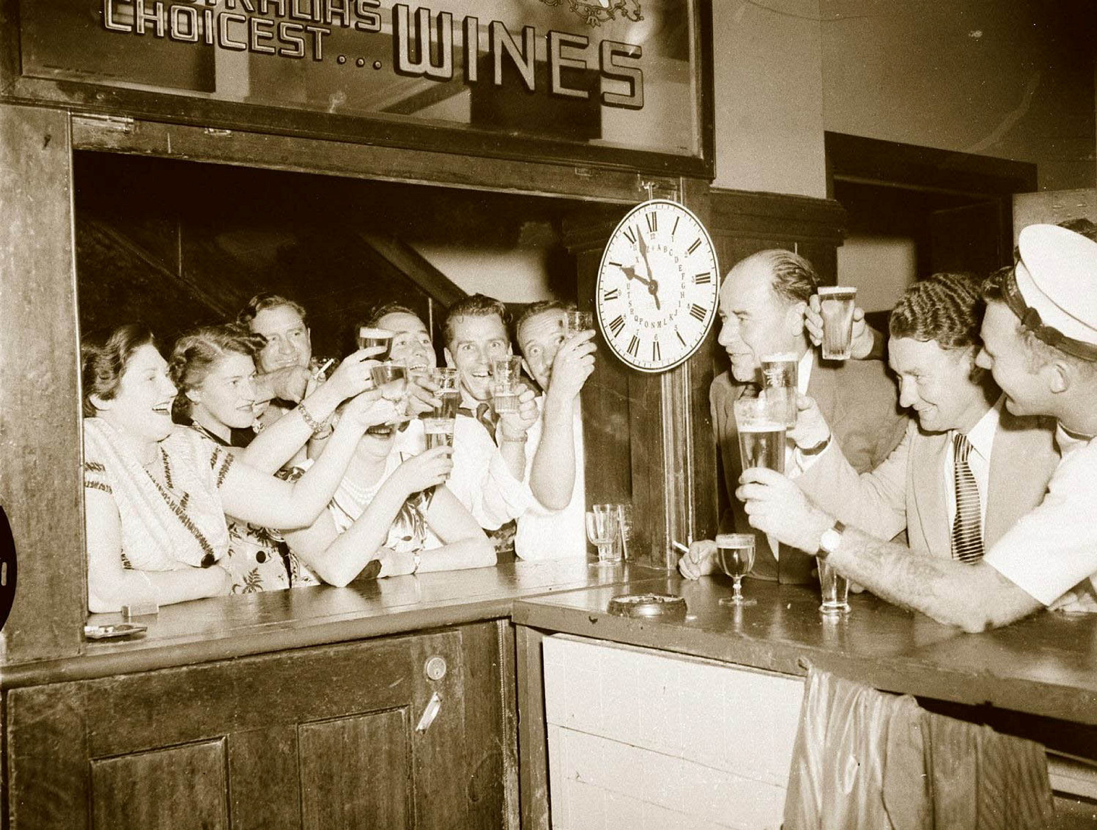 Patrons, drinks raised, crowd a pub bar with a clock showing 10 pm.