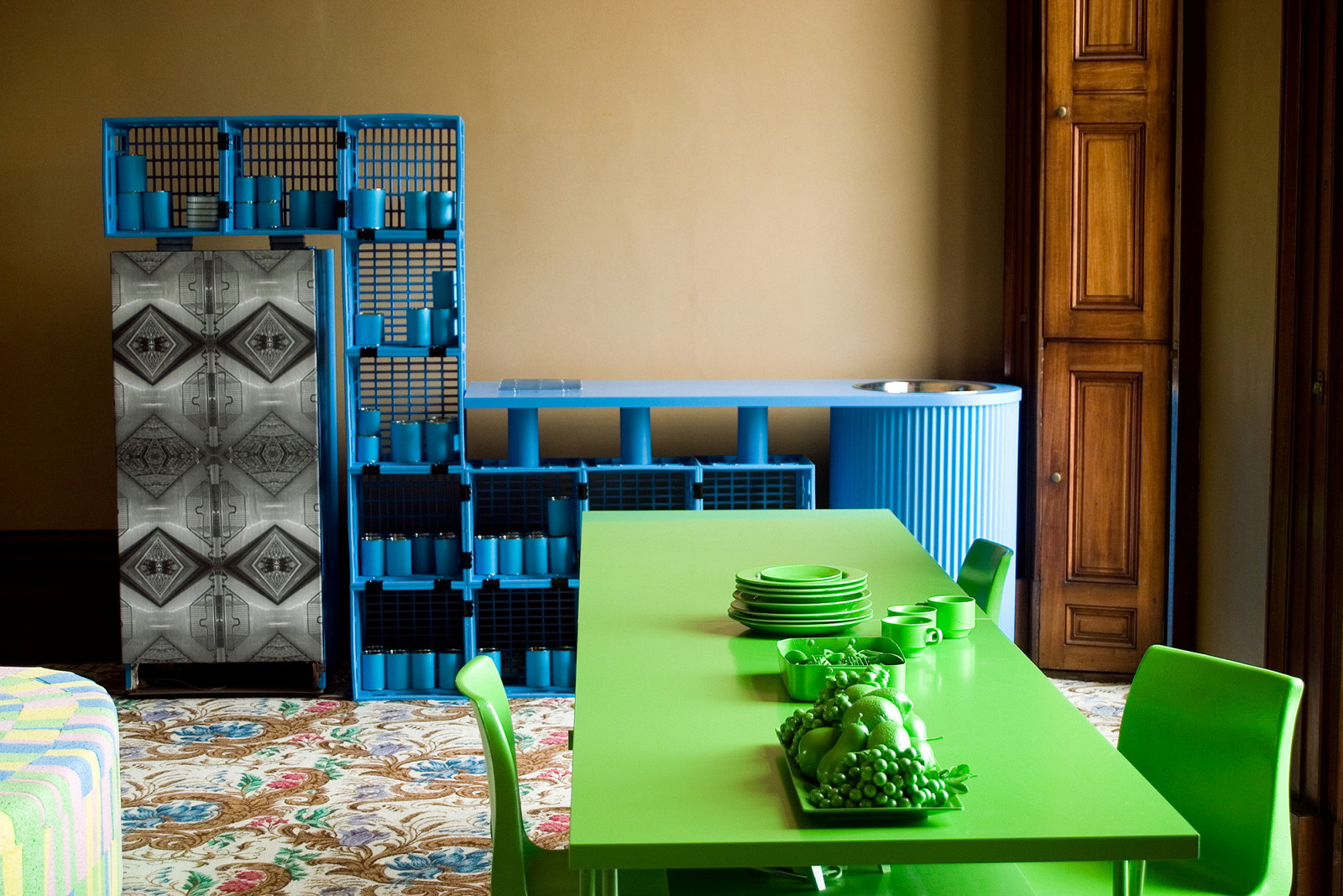 A green table with green plates and cutlery in front of a blue structure made from milk crates
