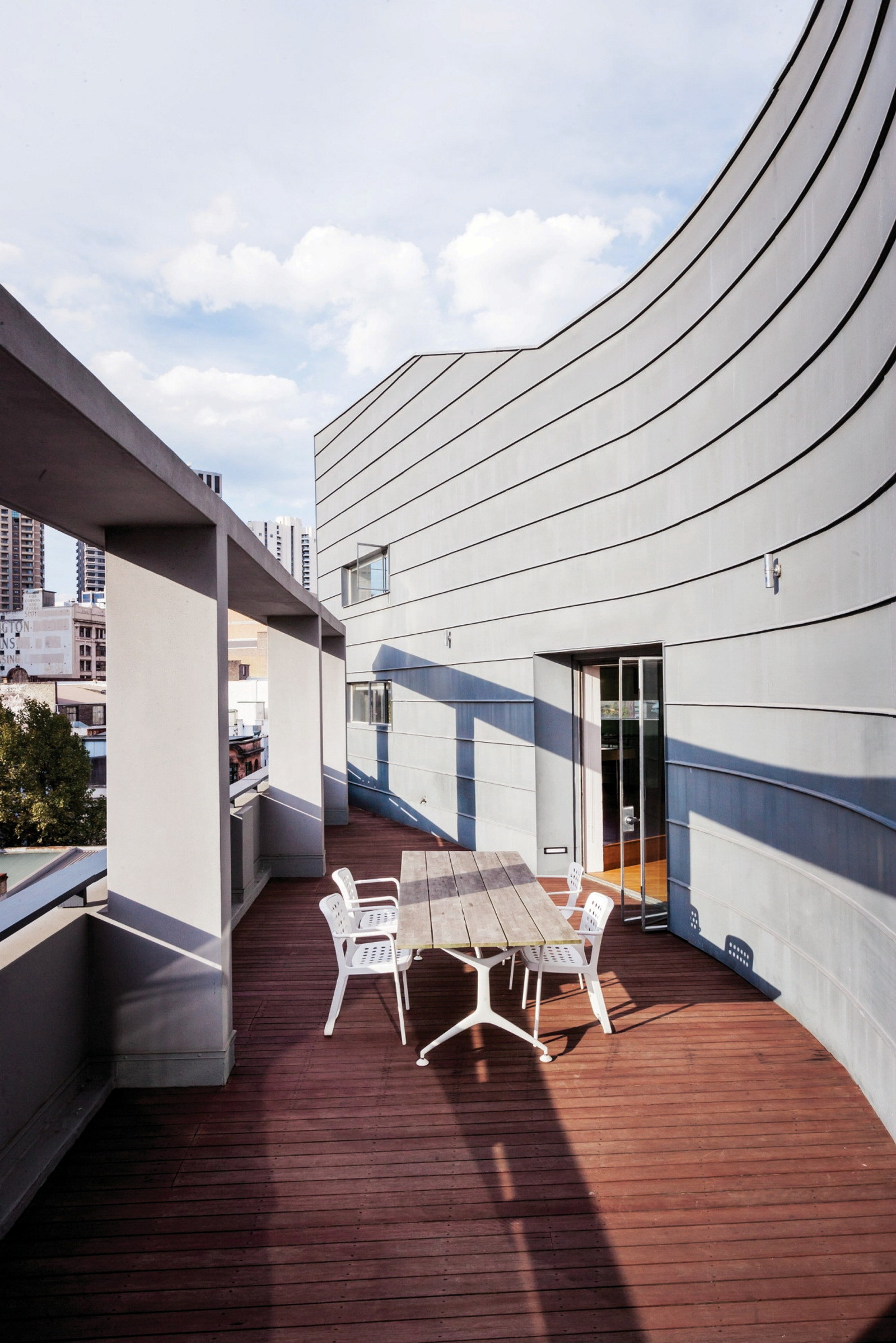 The outdoor terrace with wooden floorboards, table setting and exterior zinc cladding. The brise soleil (French for sun breaker) casts a shadow across the terrace