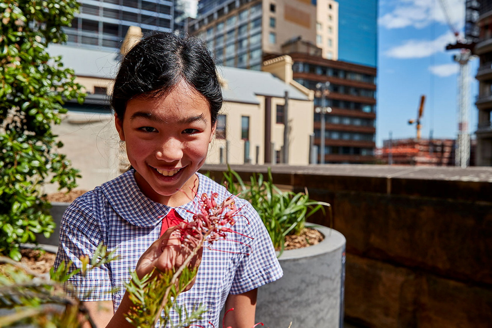 Girl in school uniform eating plant with museum and city buildings in background.