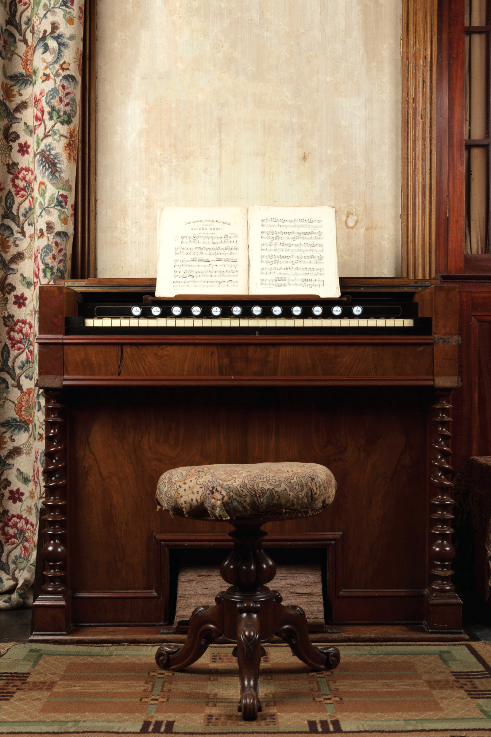 Harmonium viewed straight on, with stool and music book open on stand.