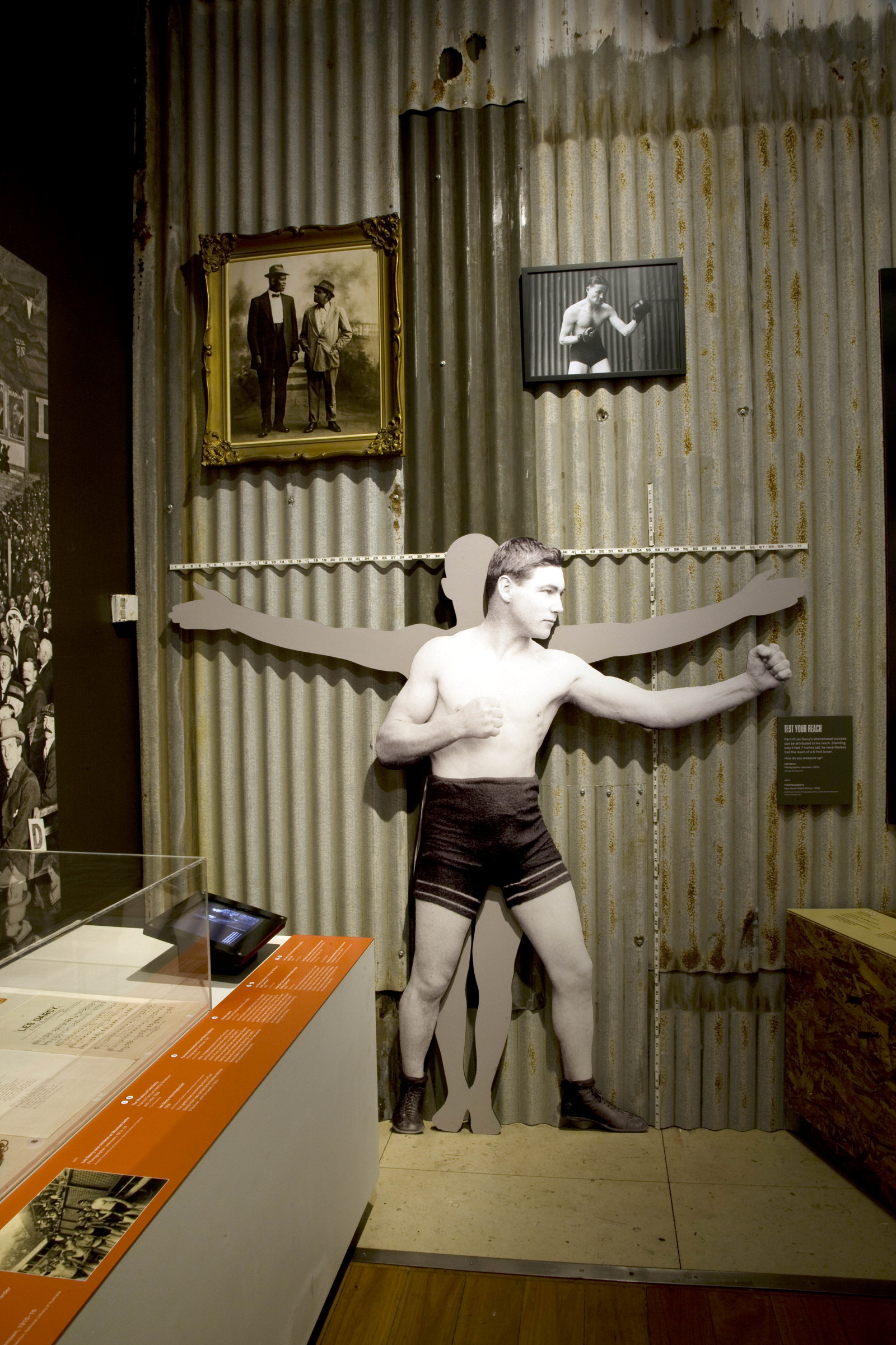 Wall lined with corrugated iron and cut out figures of boxers.