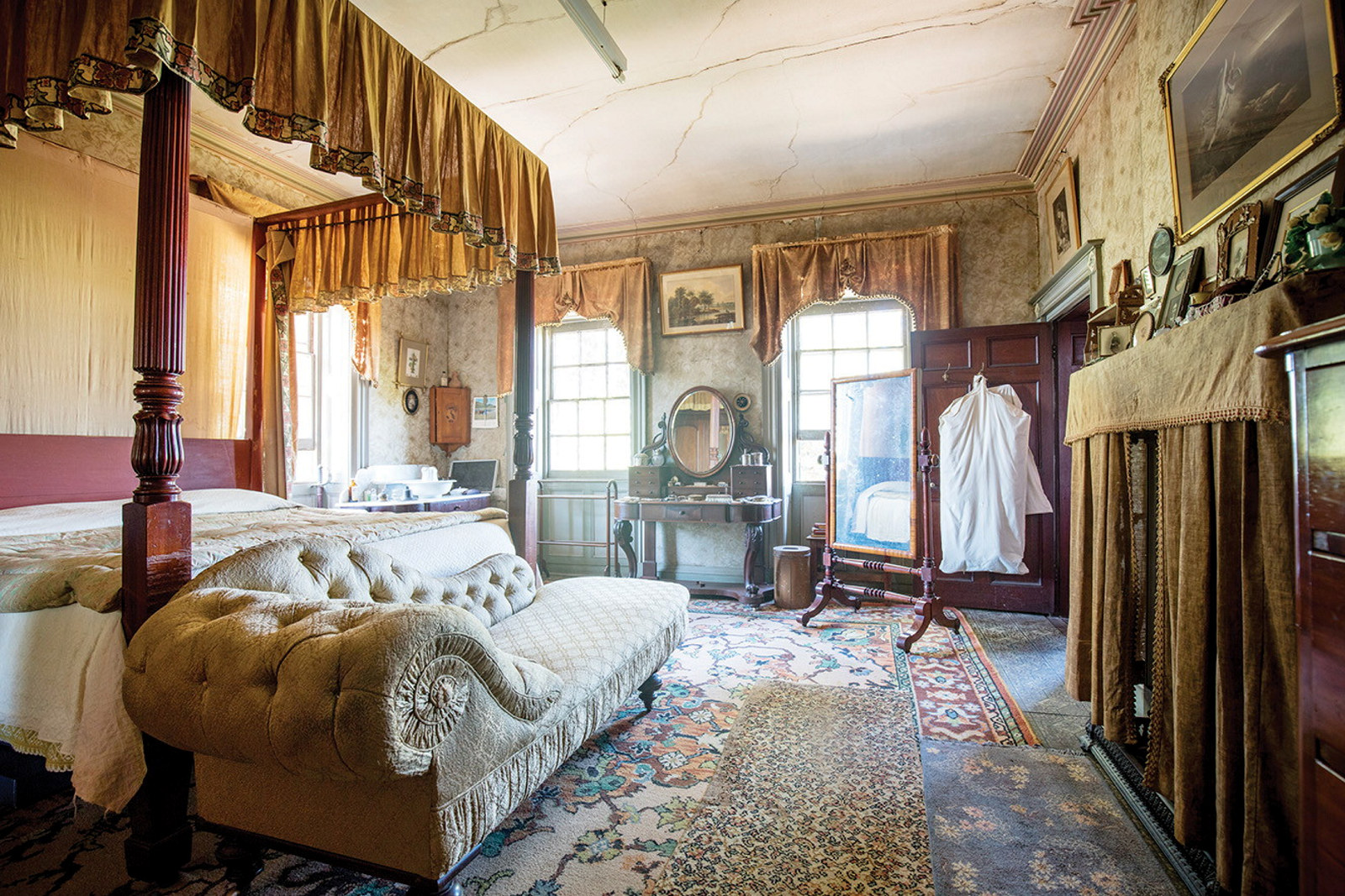 Ornately furnished bedroom with canopied bed and chaise longue to left and windows at rear.