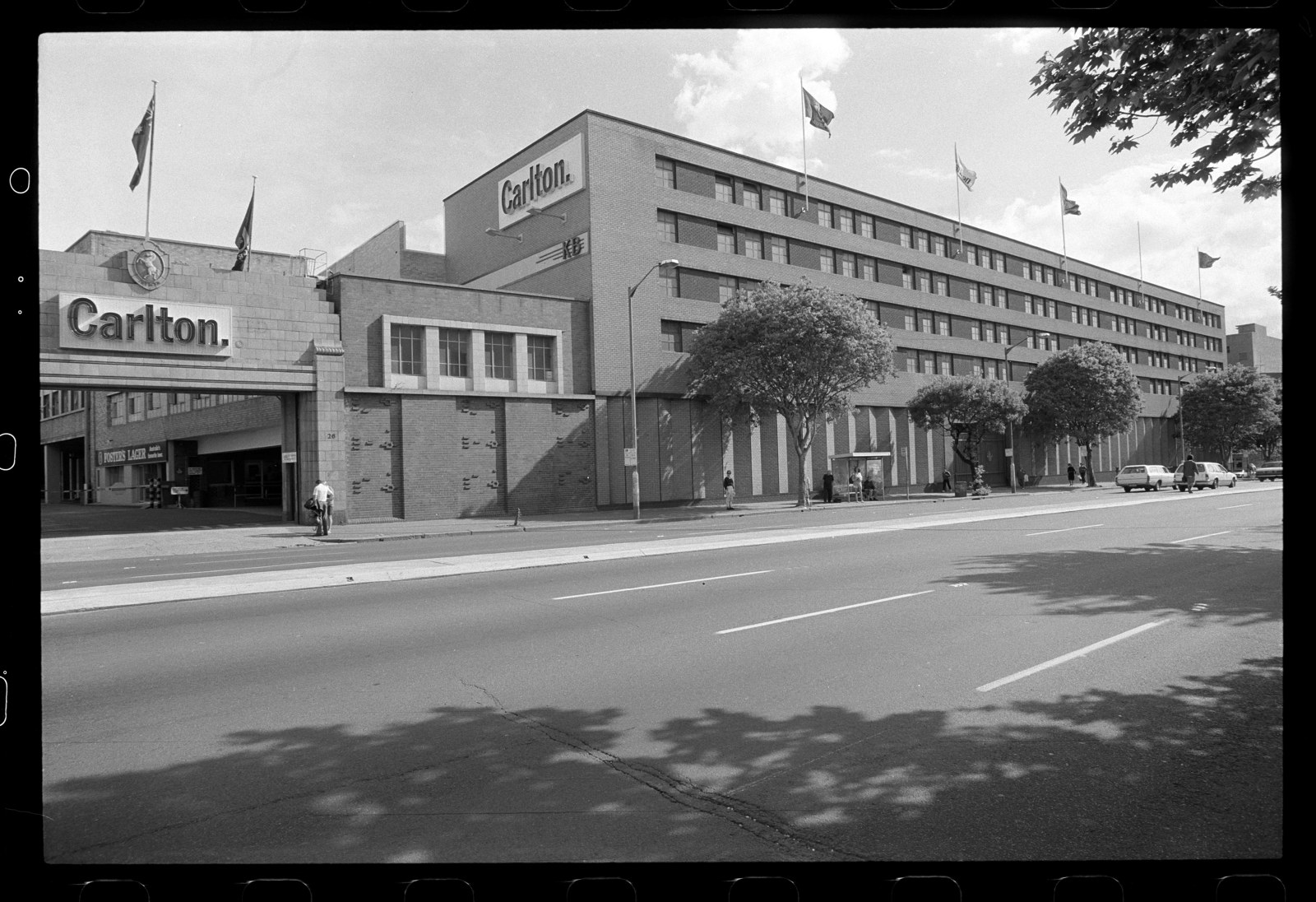 B&W image of a 5 storey building with â€˜Carltonâ€™ sign and logo above the vehicle entry. Flags are flown on the building.