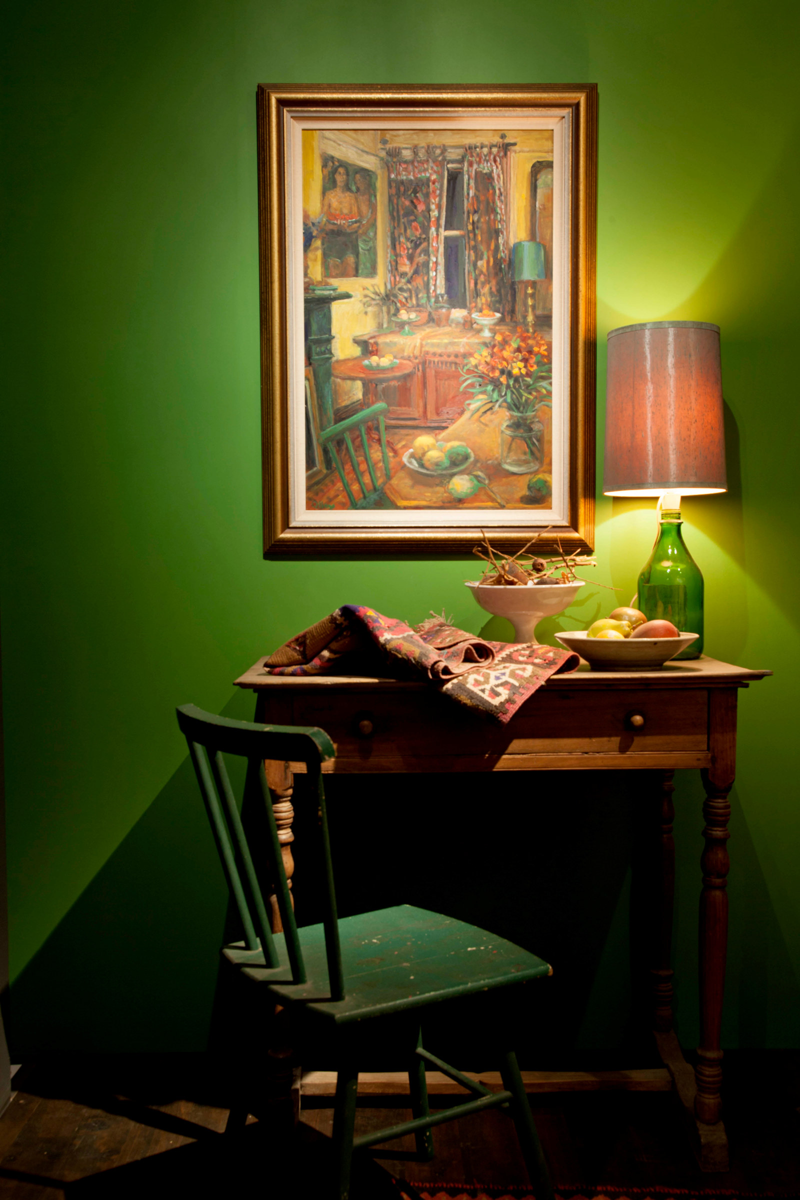Shot of chair, desk and lamp against green wall with painting above.
