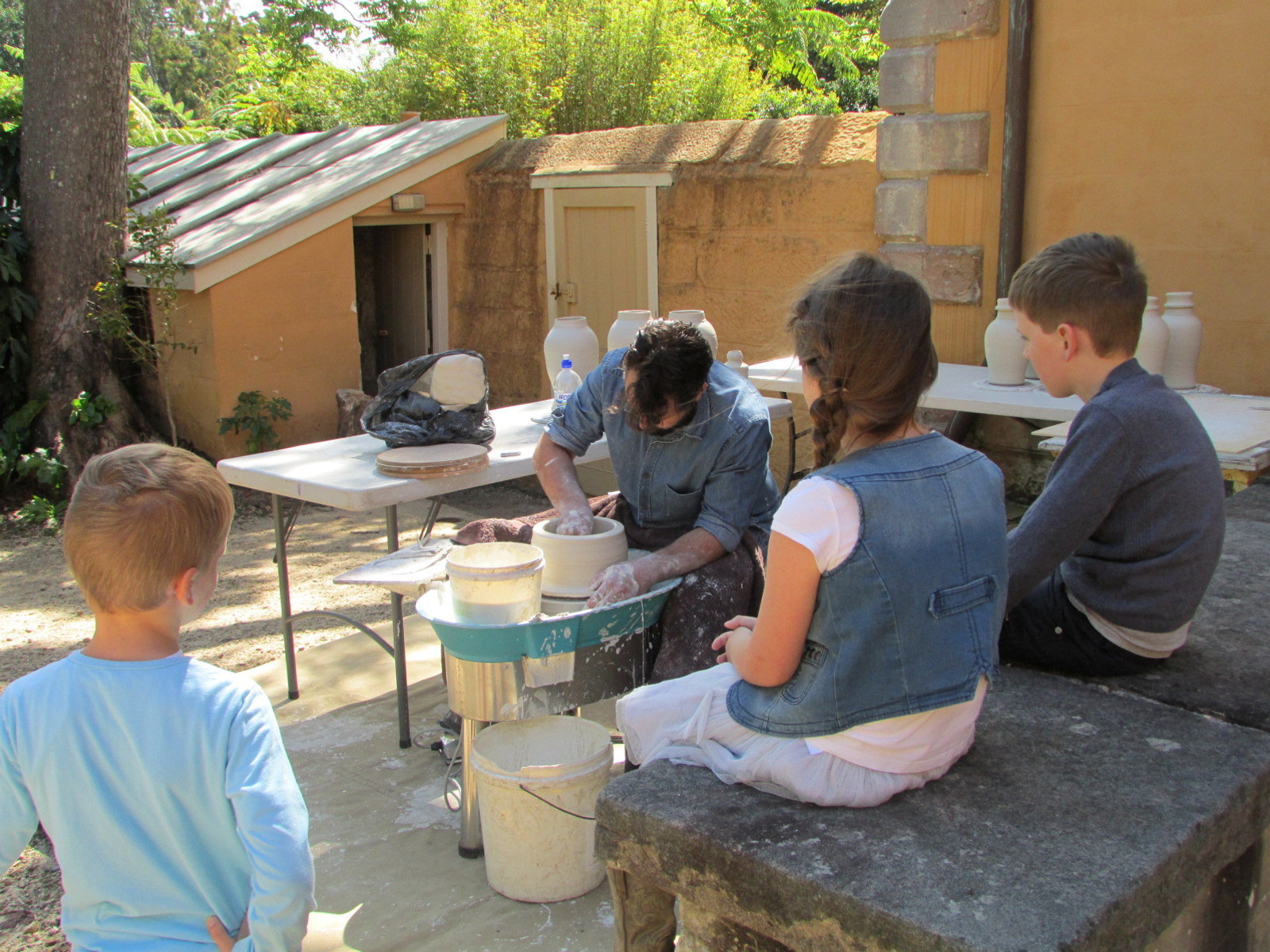 Visitors watch Andrei Davidoff at work on potter's wheel in yellow painted courtyard