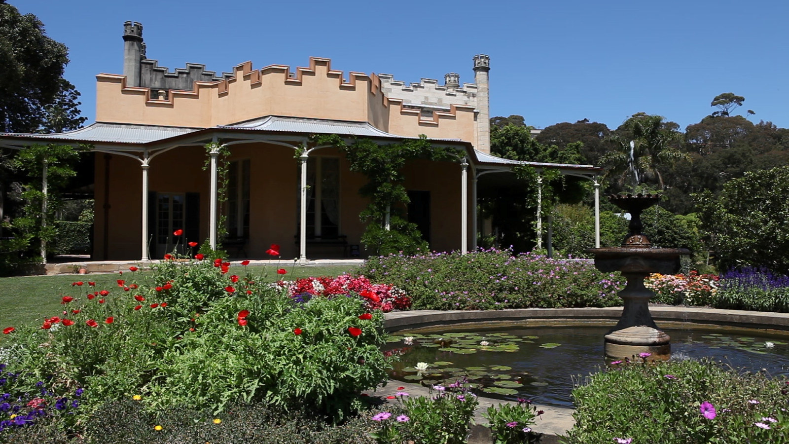 Image of the front of Vaucluse house with the gardens in full bloom. A fountain appears in the foreground squirting water.