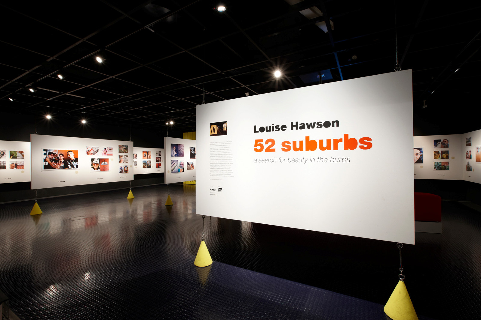 Photo of the 52 Suburbs exhibition. A large panel isin the foreground with the exhibition titlle printed on it.
