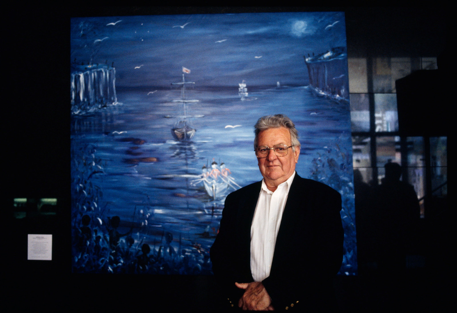 Man in front of large, mostly blue painting.