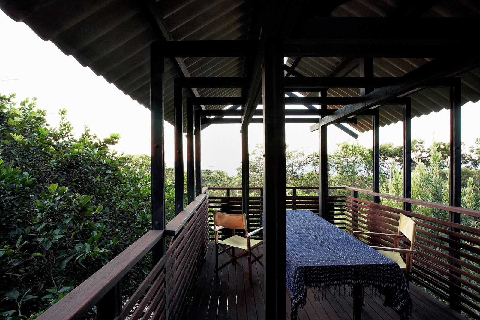 This is a photograph of a table and chairs sitting on the timber decking of the belvedere of the Mooloomba House. It has timber balustrades and a corrugated roof.