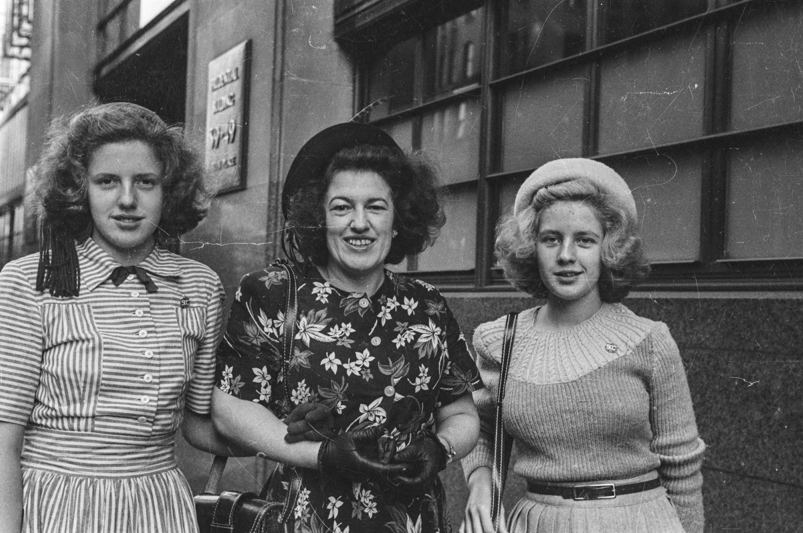 Black and white street photograph of three women linking arms walking down the street.