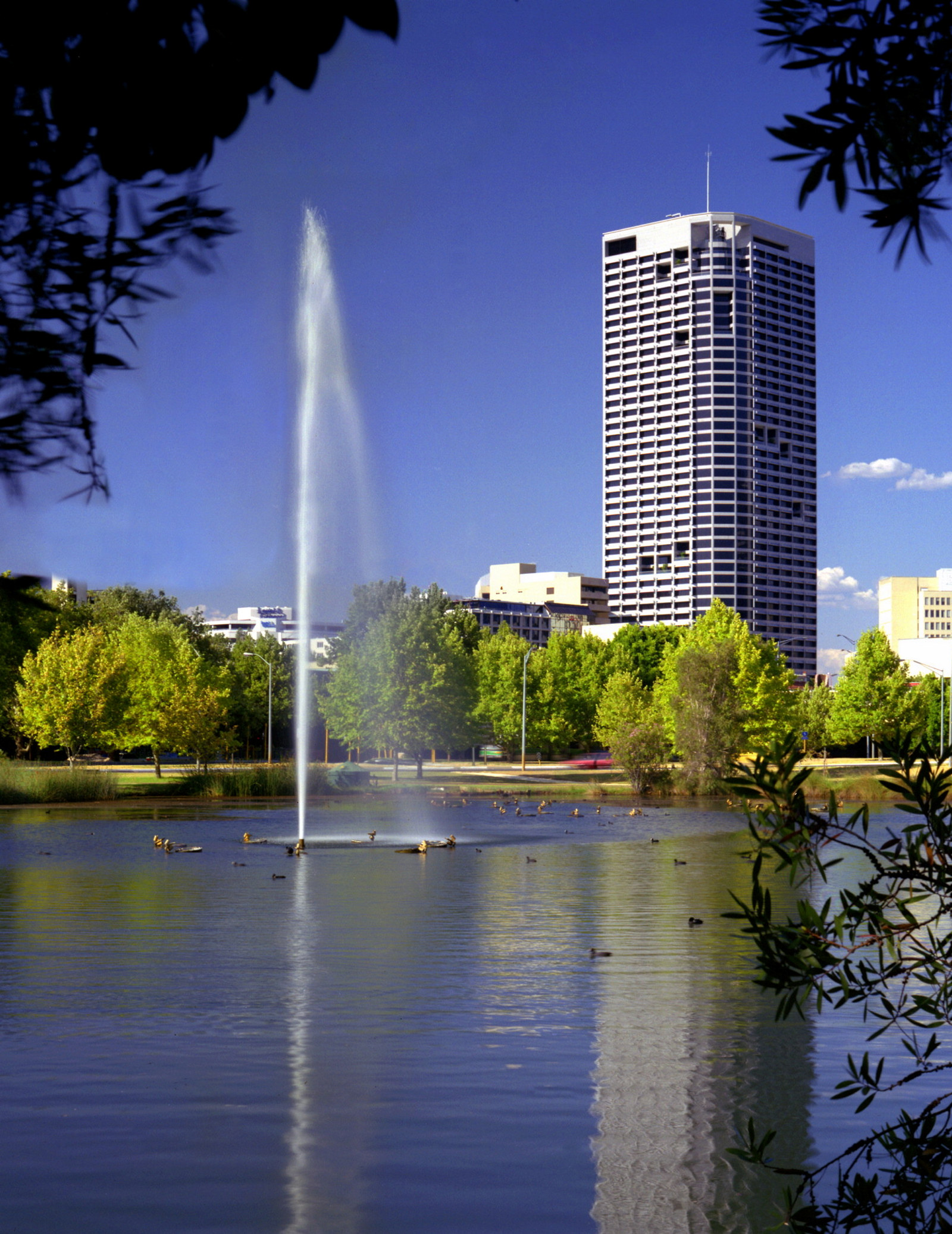 This is a colour photograph of an office tower with a wide river and fountain of water in the foreground