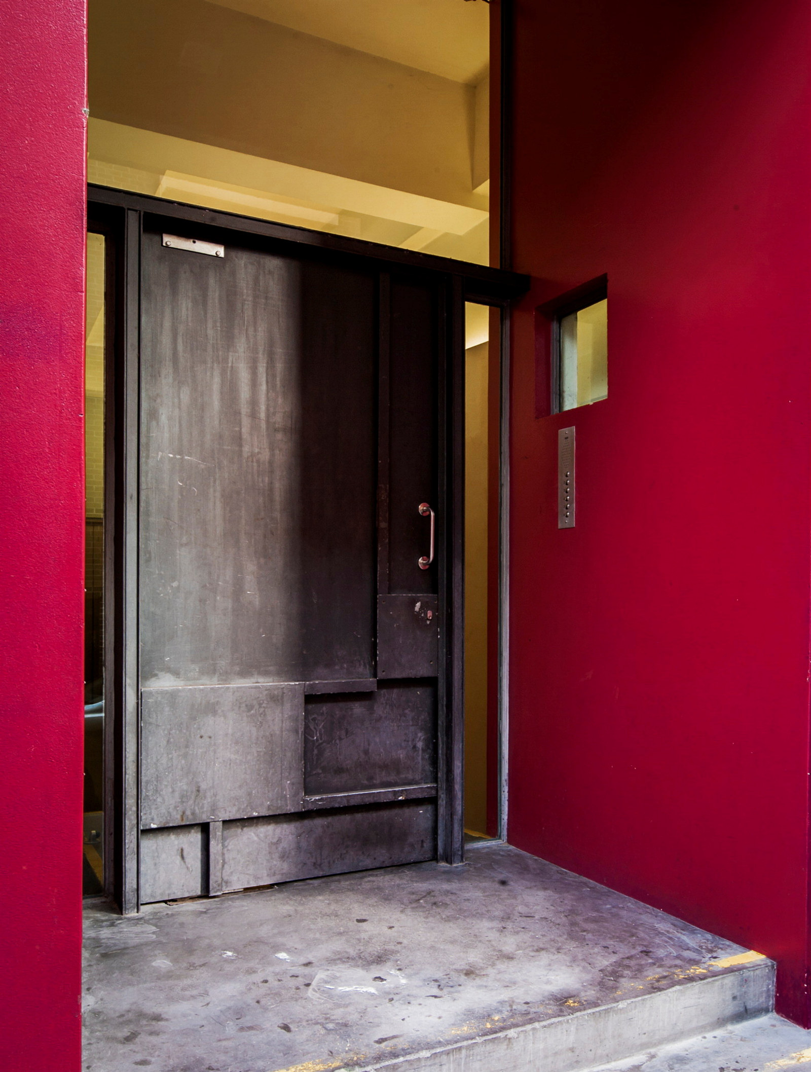 Exterior photograph of the steel-plated front door of the Droga apartment featuring a strong pink-coloured surround