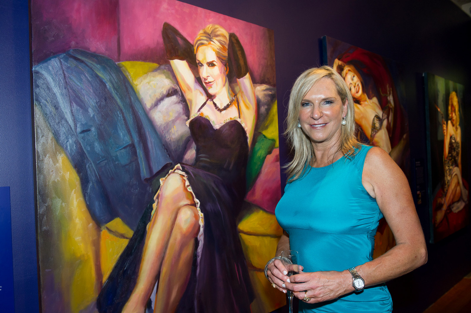 Skye Leckie wearing a blue dress and standing in front of her portrait She Couldn't be Good, at the opening of Wicked Women: an exhibition by Rosemary Valadon