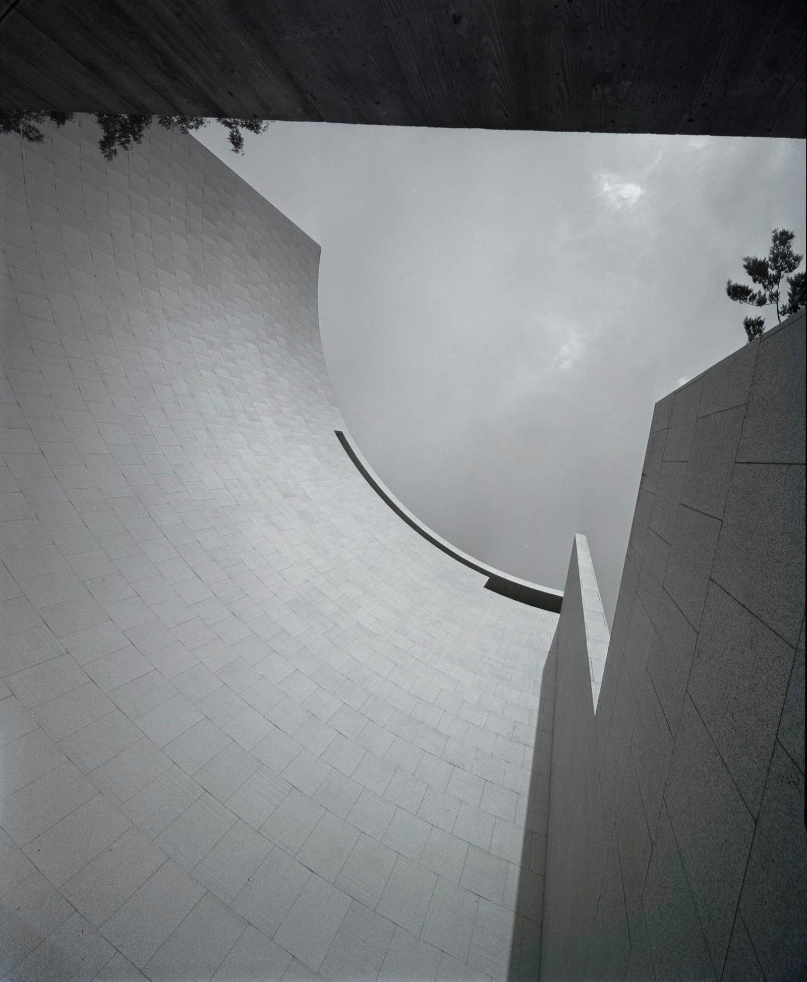 This is a black and white photo of a building facade shaped in a curved quadrant and taken from the base of the building looking up