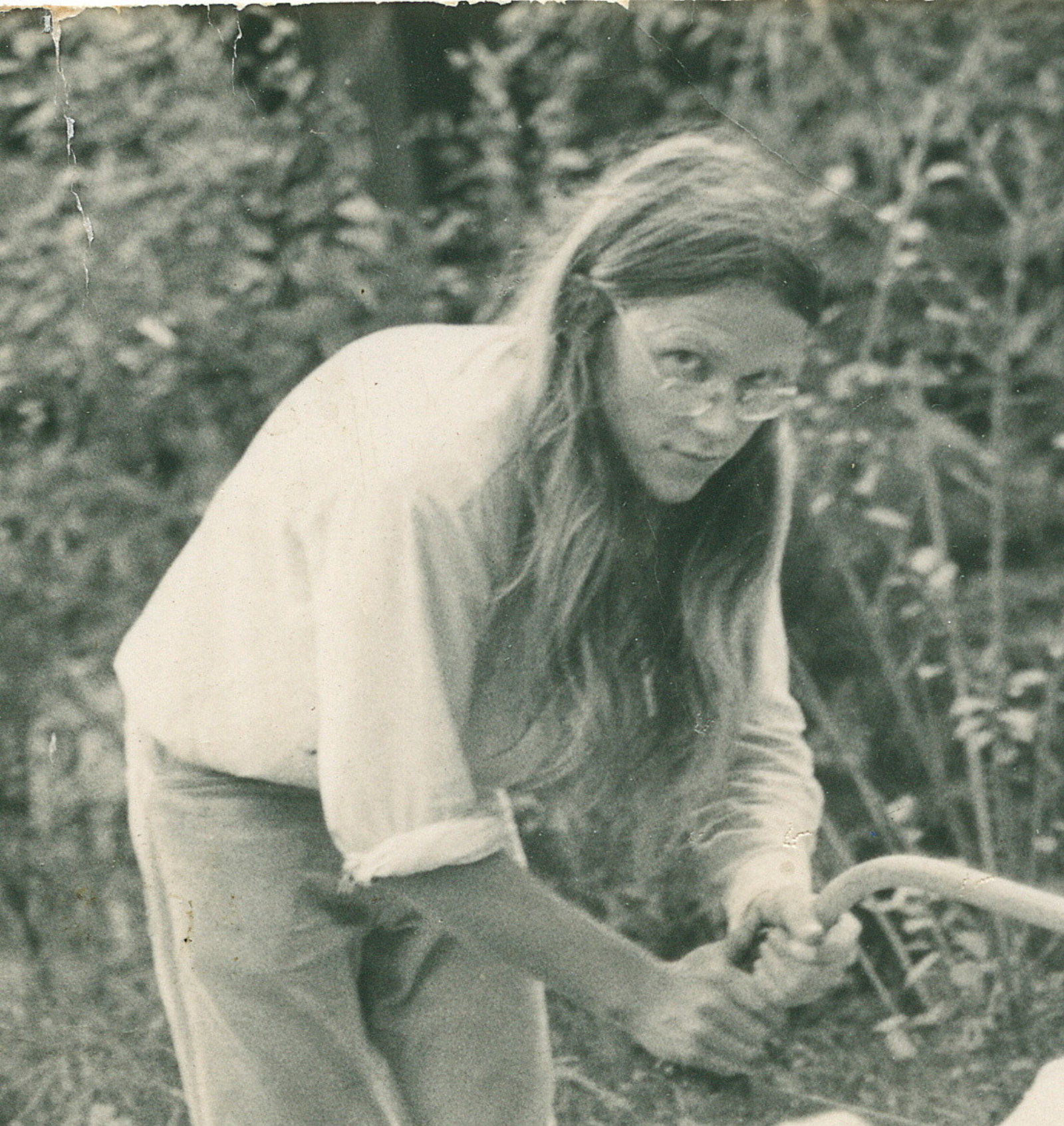 Black and white photo of young man using saw in garden setting.