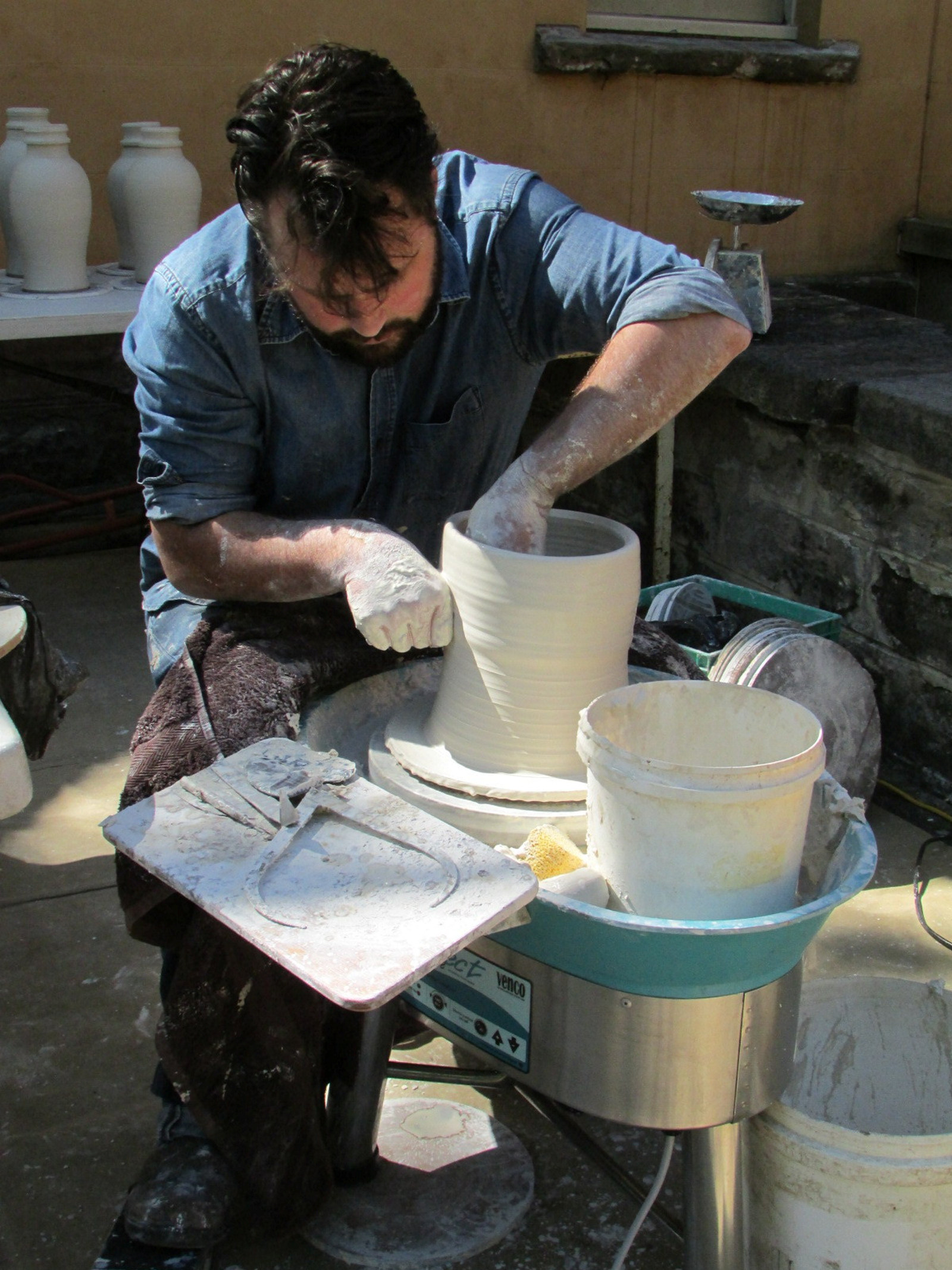 man turning white ceramic vessel on potters wheel